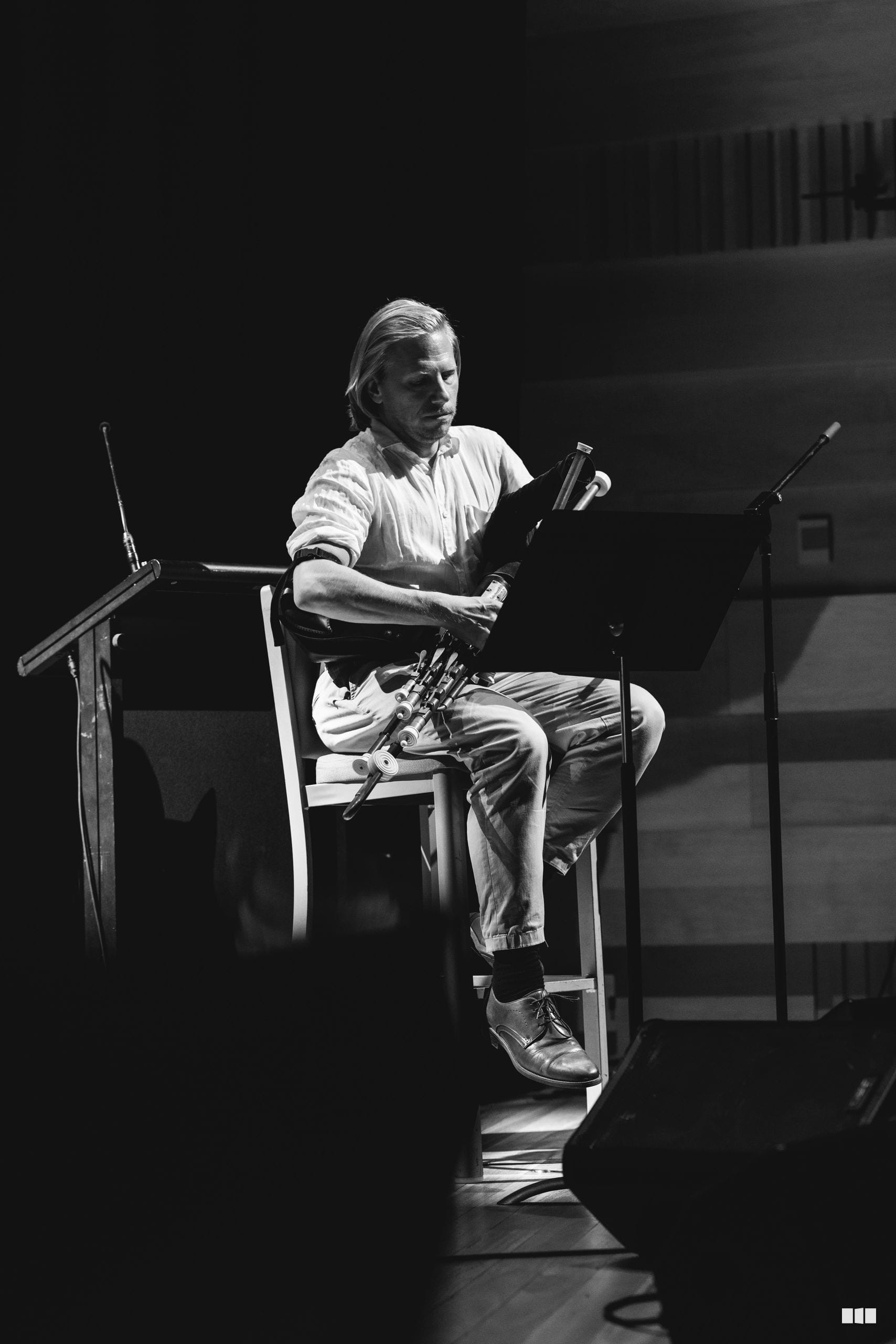 A musician seated and playing trumpet during a solo performance on stage with microphones positioned nearby.