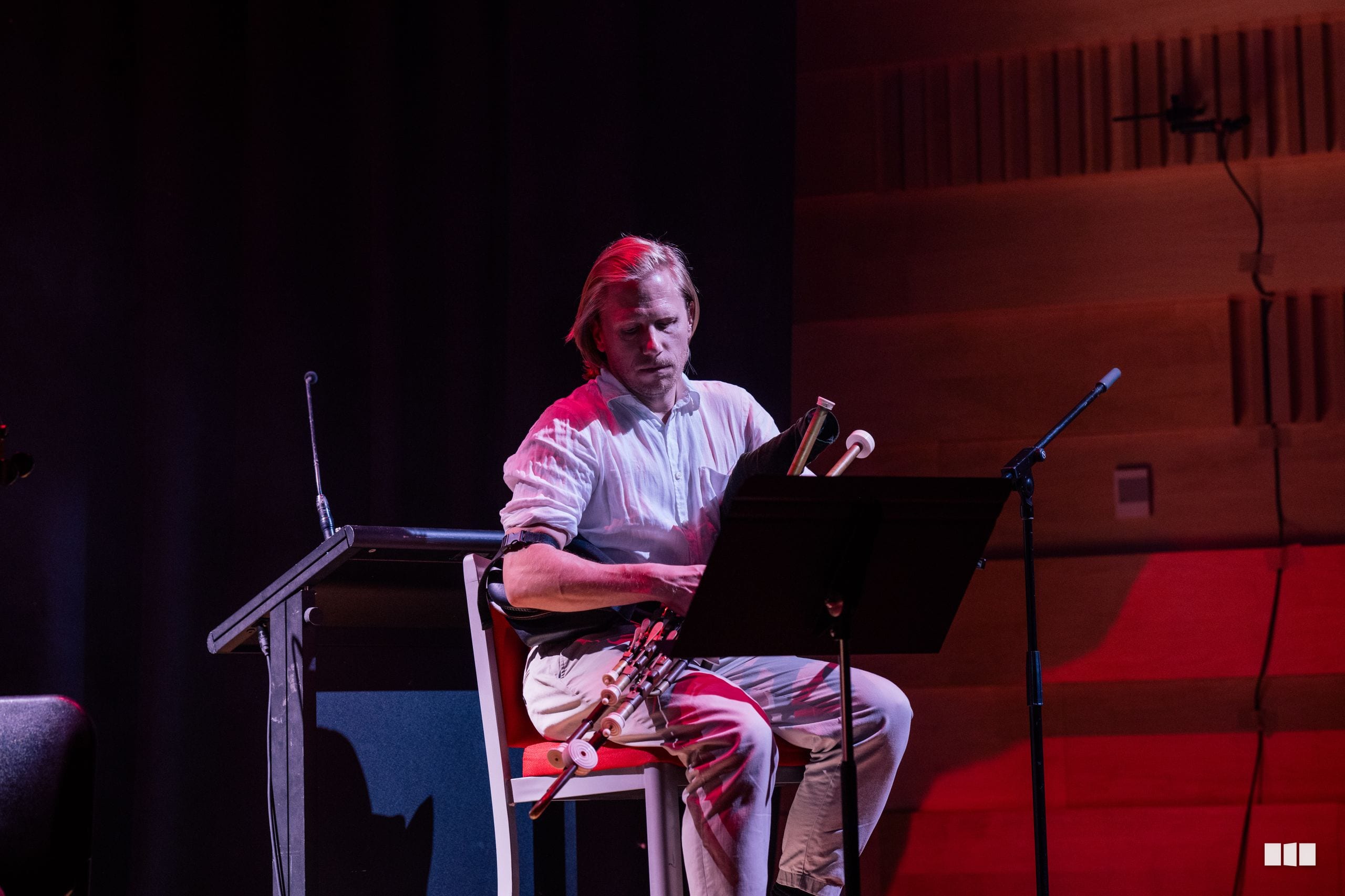 A musician performs on a wind instrument while reading from a laptop during an orchestral performance.