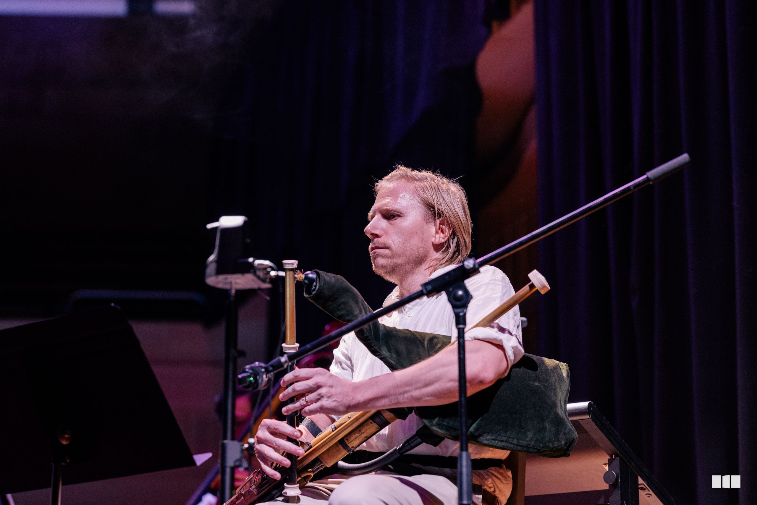 A musician plays a wooden wind instrument while seated on stage during a performance.
