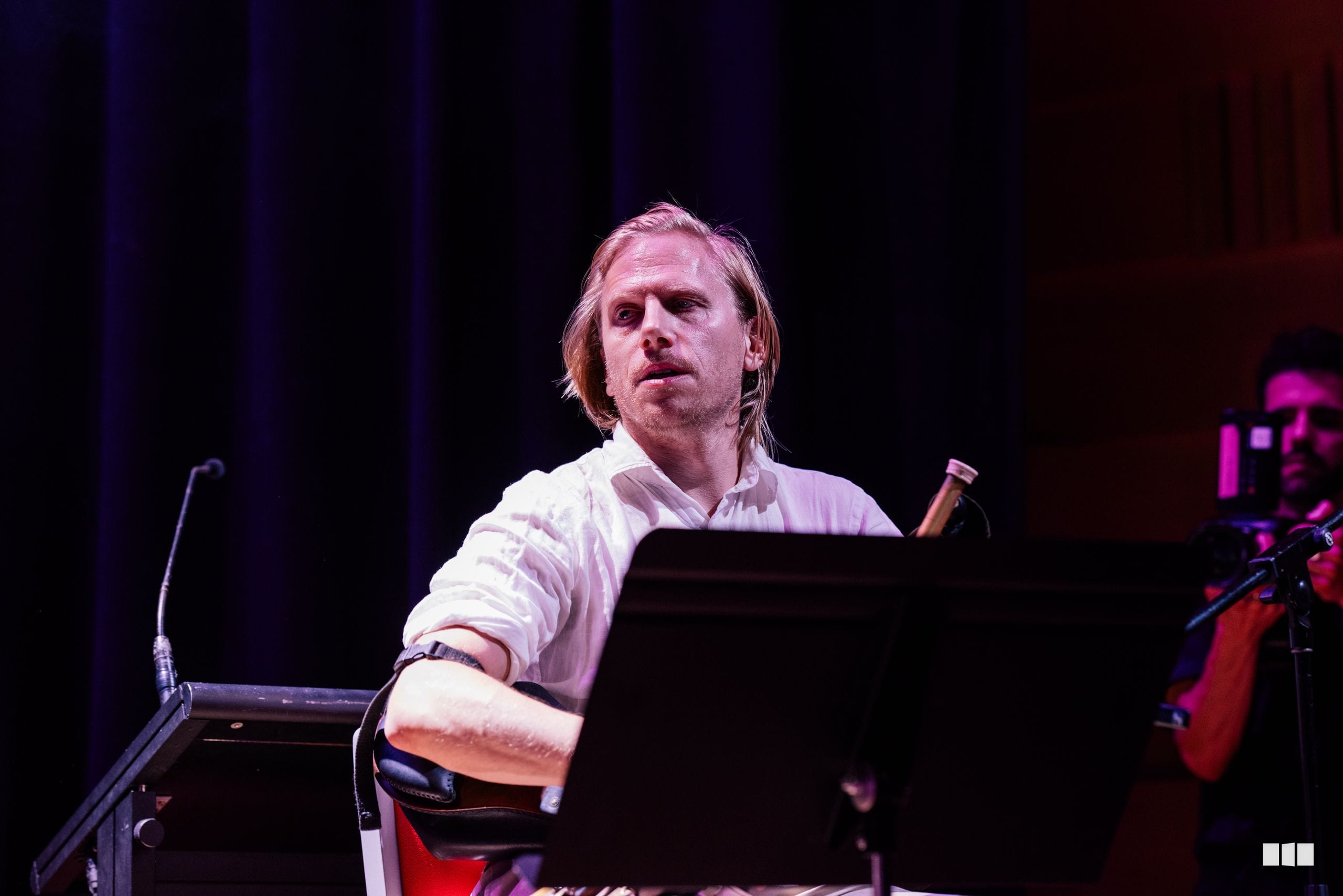 A pianist performs at the keyboard during an orchestral concert under stage lighting.