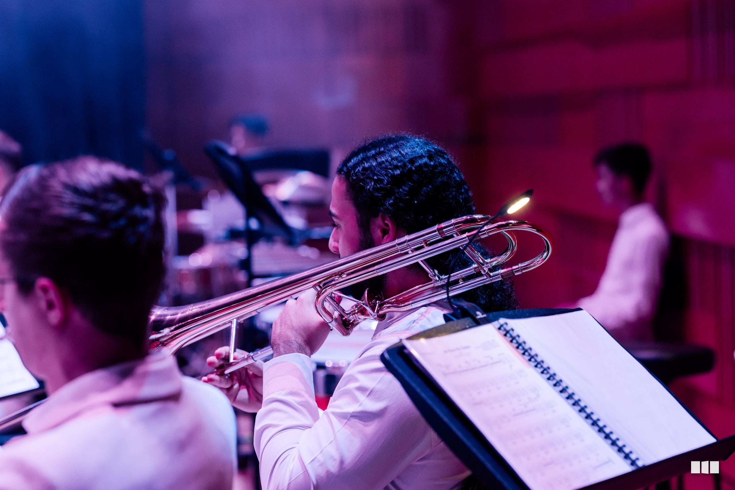 A trombonist in formal attire performs with sheet music during an orchestral rehearsal or concert.