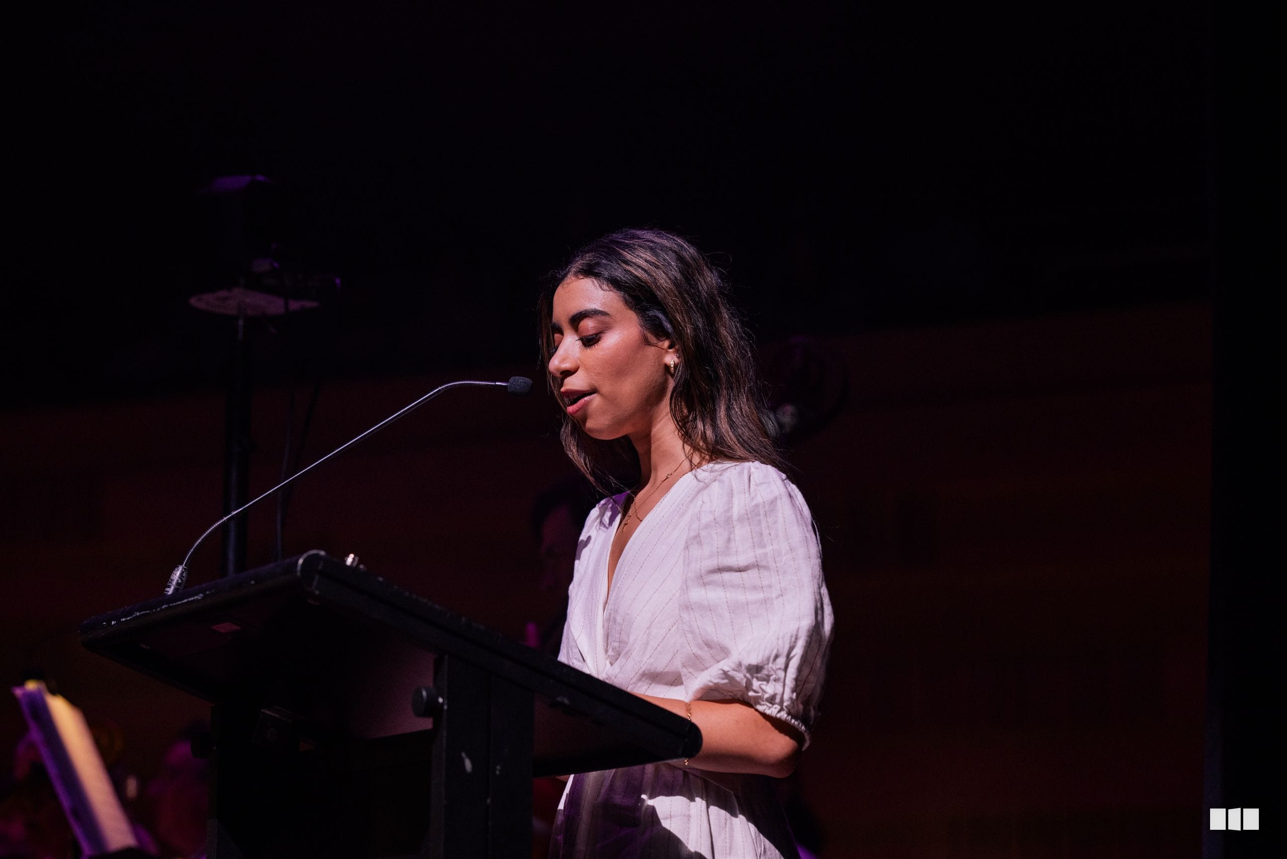 A female soloist performs at the microphone on stage with atmospheric purple lighting in the background.
