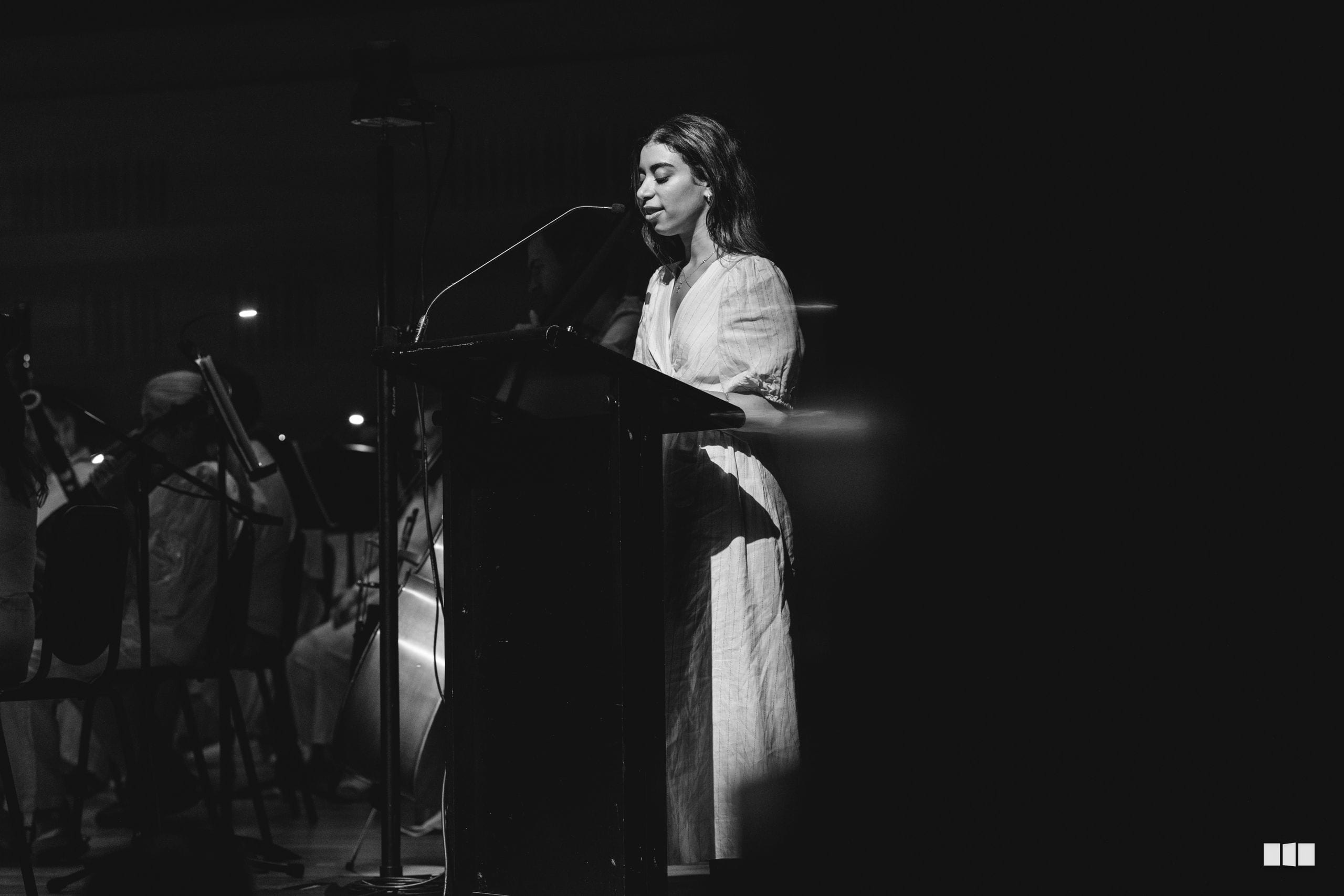 A female soloist performs at the microphone in an elegant white blouse during a classical music performance.
