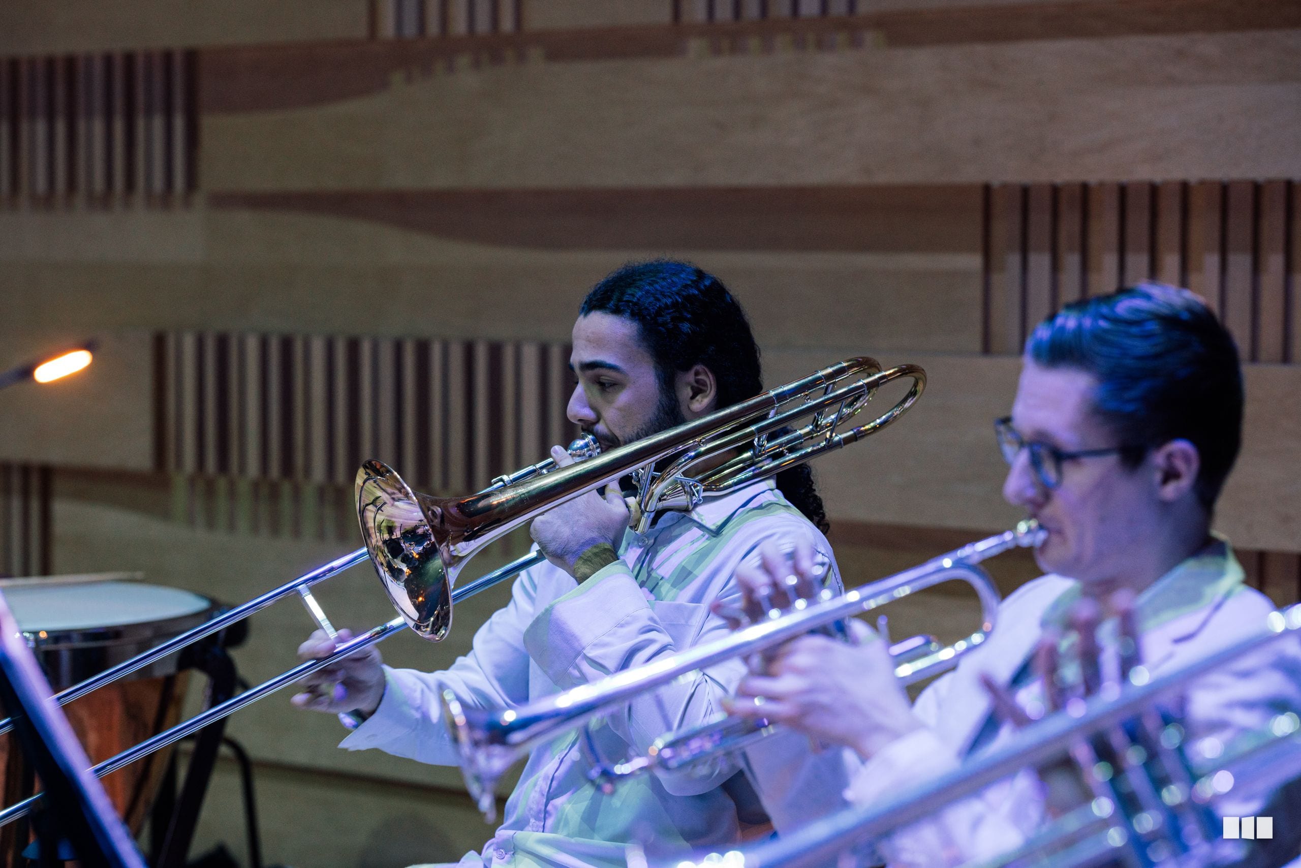 Trombone players perform together during an orchestral rehearsal or concert in a modern venue.