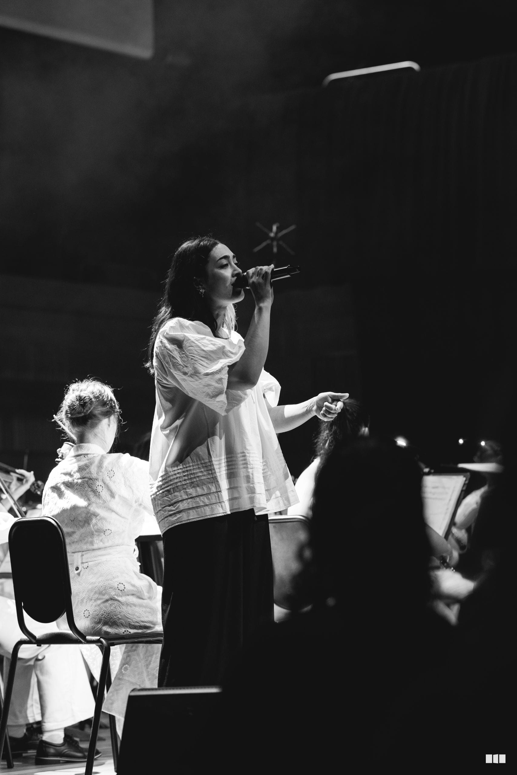 A female soloist performs at the microphone while a young choir member sits beside her during a choral performance.