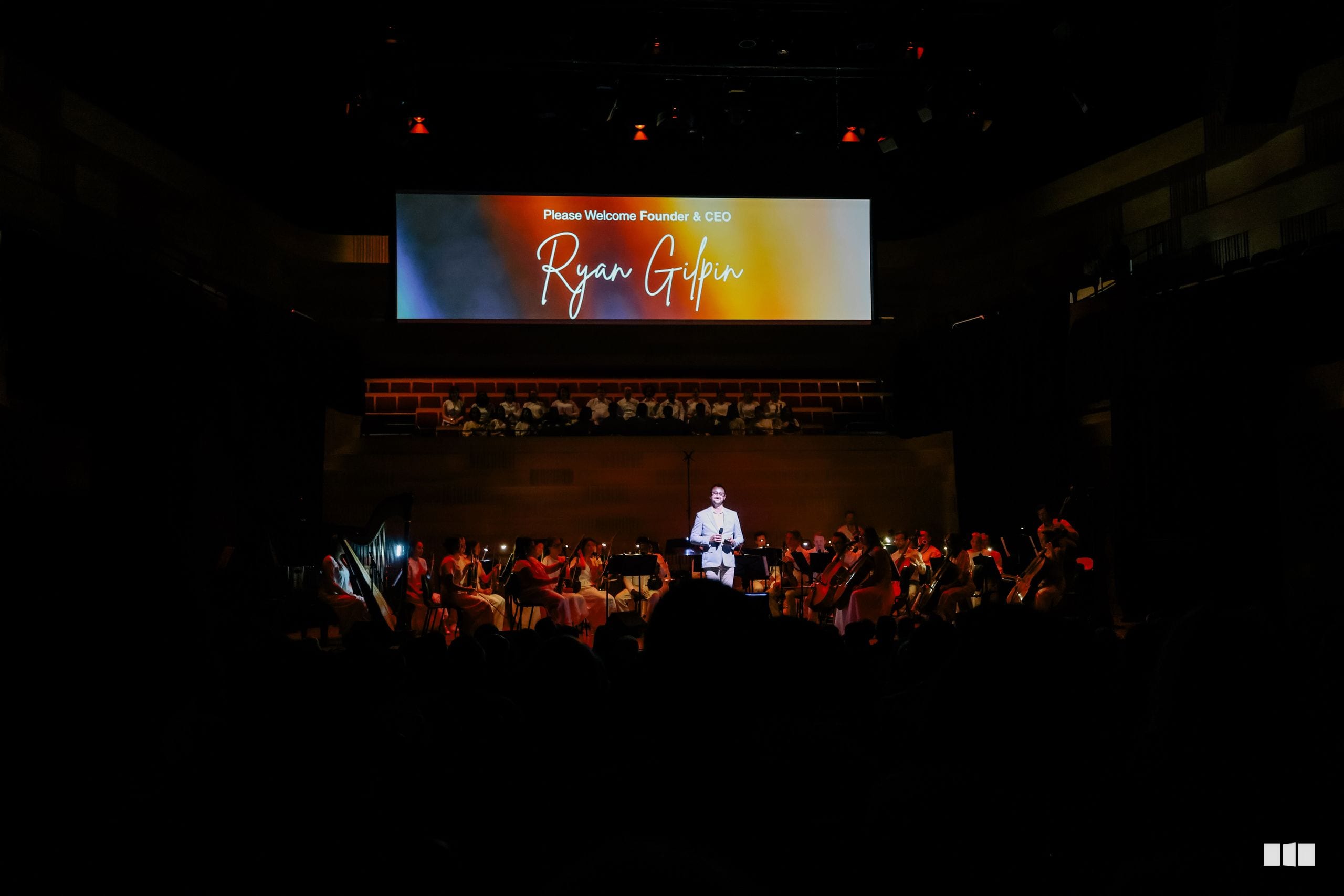 Founder and CEO Ryan Giffin is welcomed to the stage at a formal orchestral event with musicians and audience members present.