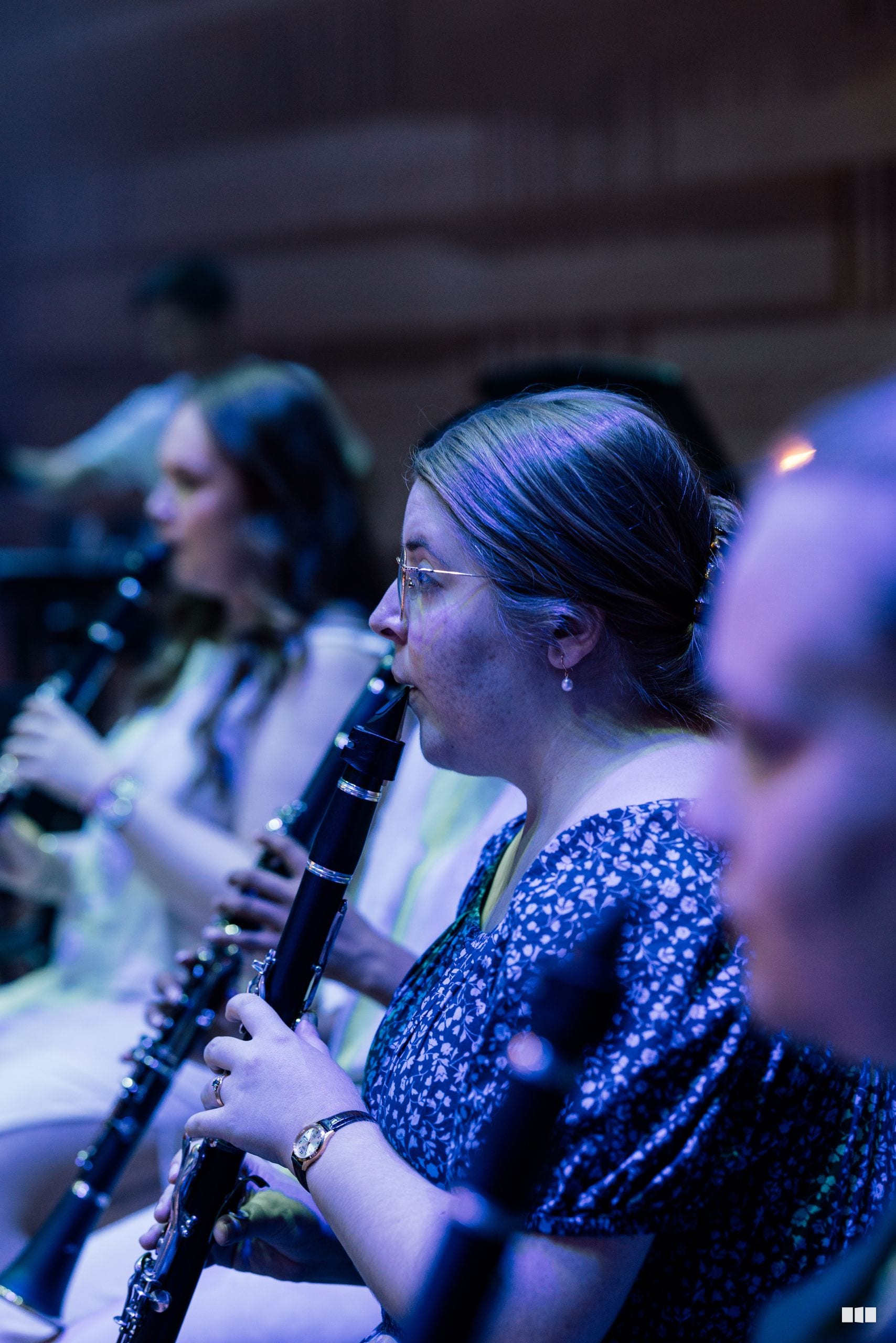 A woodwind musician plays oboe or clarinet during an orchestral performance, illuminated by blue stage lighting.