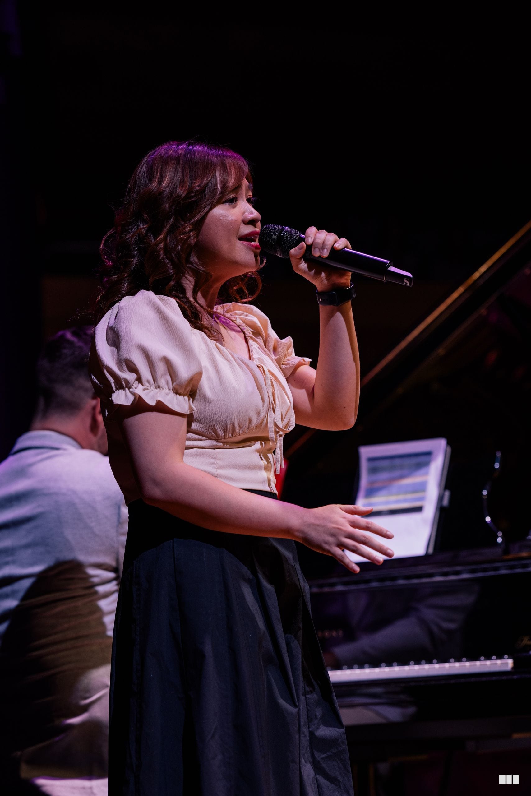 A female soloist performs at the microphone with piano accompaniment visible in the background during an evening concert.