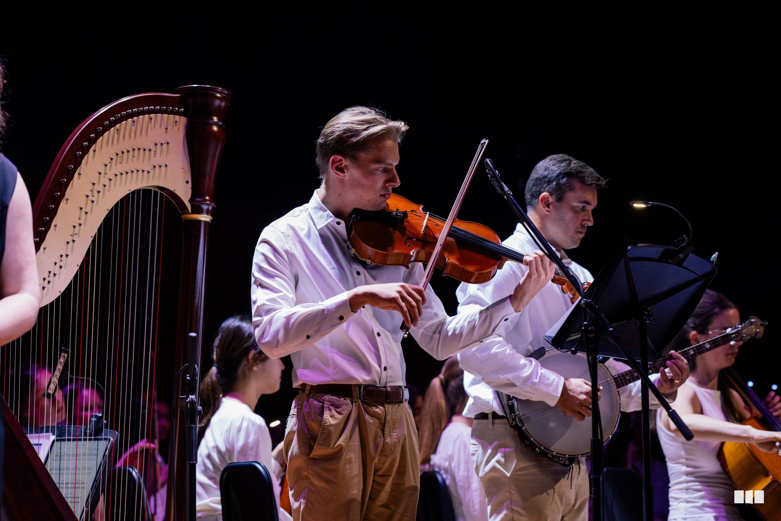 Young violinist performs alongside harp and other ensemble musicians on stage during an orchestral concert.