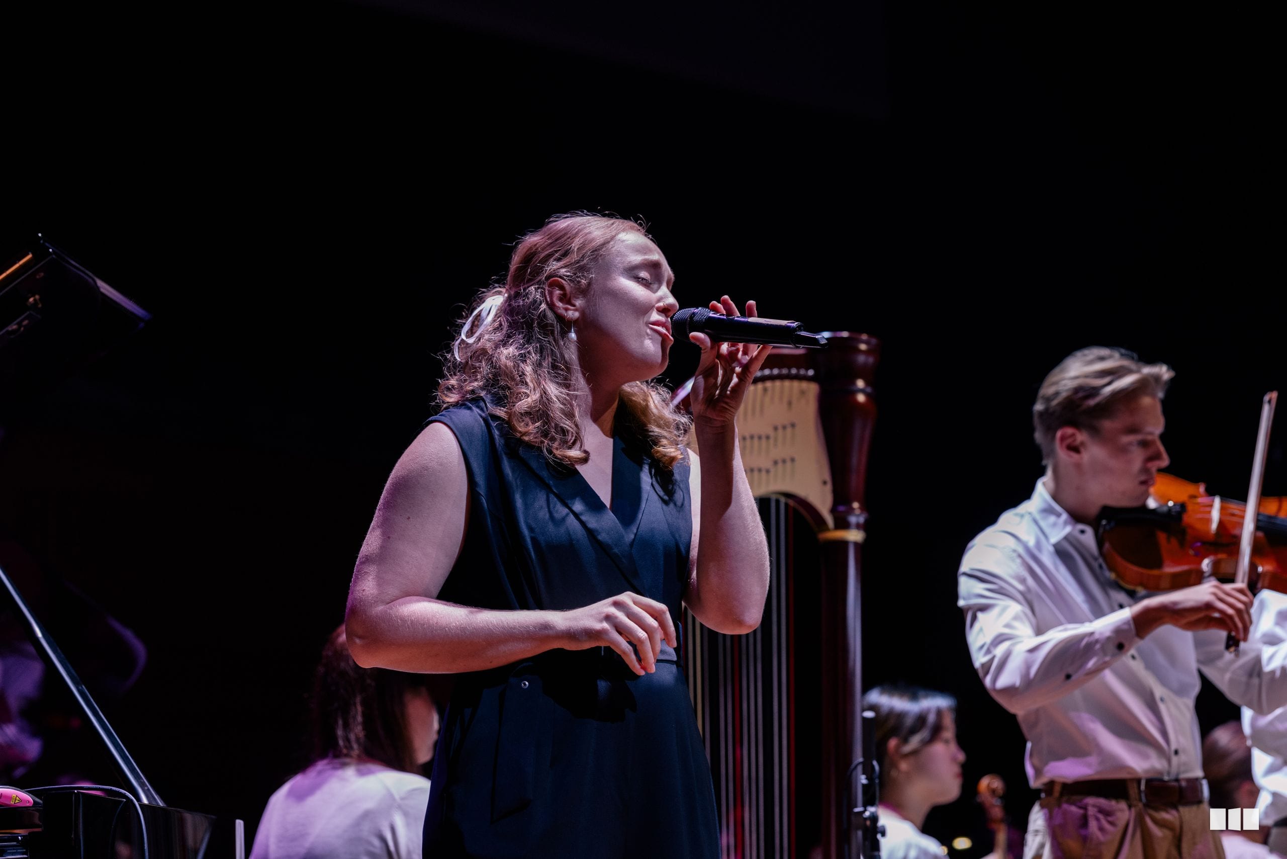 A female soloist performs with microphone while a violinist accompanies her on stage.