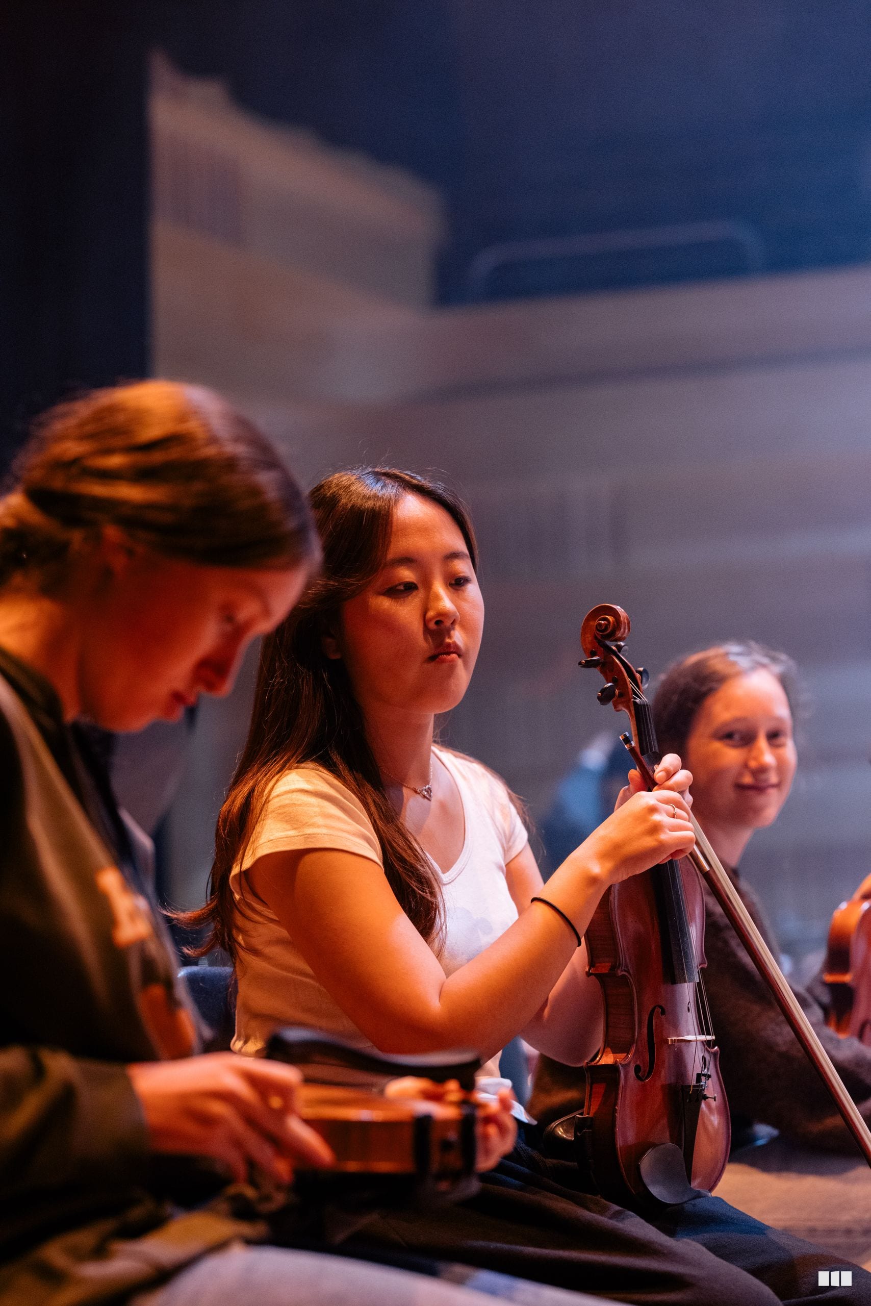 Young string players perform together on stage during an orchestral rehearsal or concert.