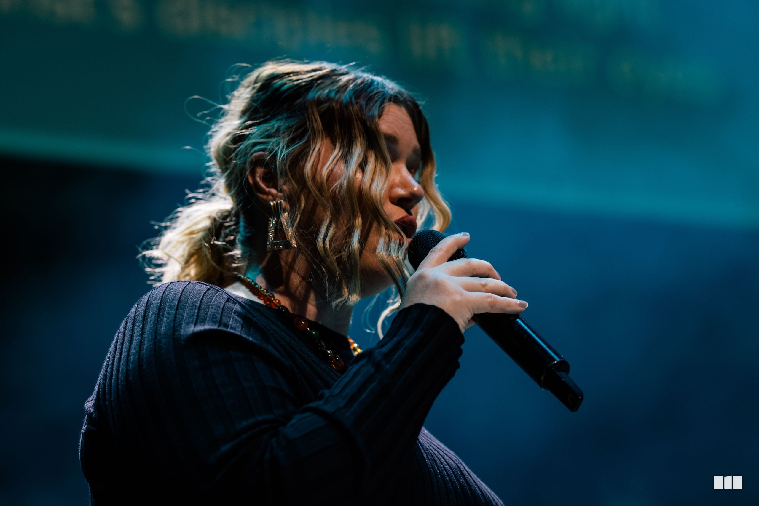 A soloist performs at the microphone against a blue backdrop during a choral performance.