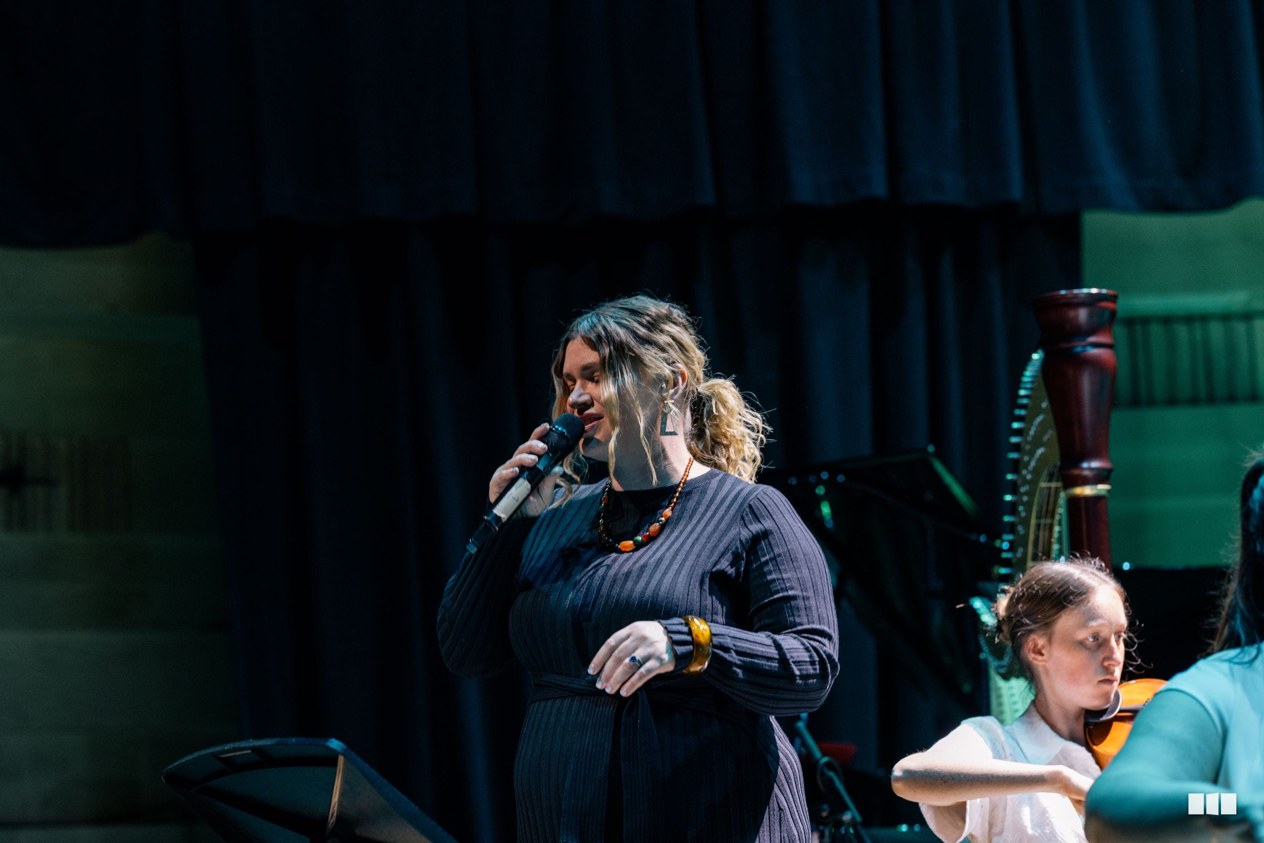 A female soloist performs at the microphone during a choral performance on stage.