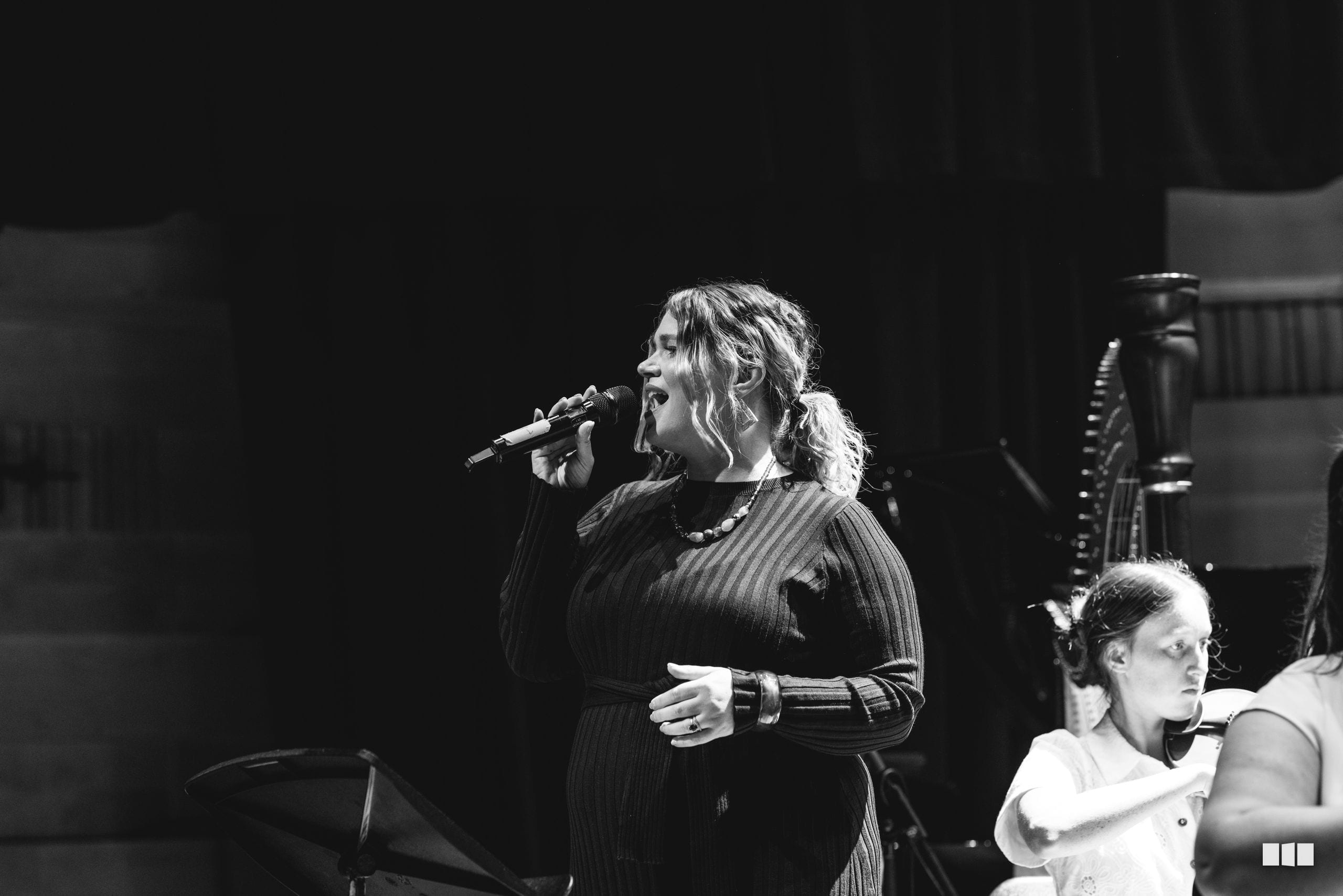 A solo female vocalist performs passionately at the microphone in a black pinstriped dress during a choral performance.