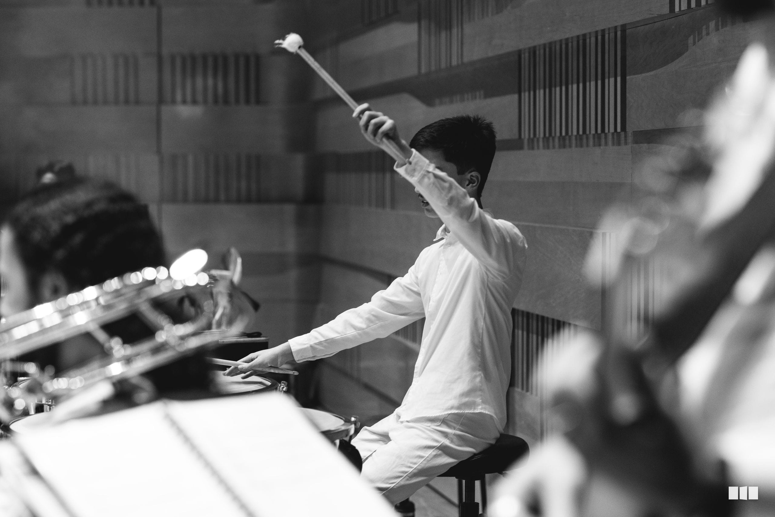 A young musician conducts with raised baton while seated at the keyboard during an orchestral rehearsal or performance.