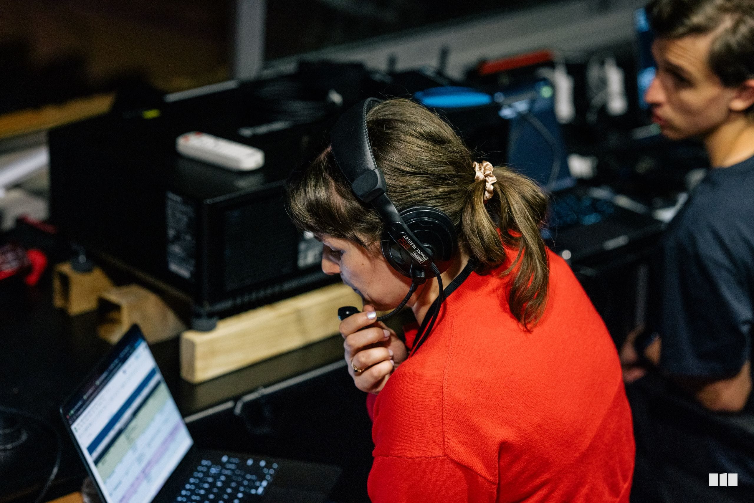 A young person wearing headphones and a red shirt operates audio equipment at a mixing console during a recording or broadcast session.