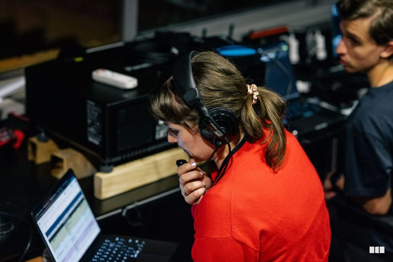A young person wearing headphones and a red shirt operates audio equipment at a mixing console during a recording or broadcast session.