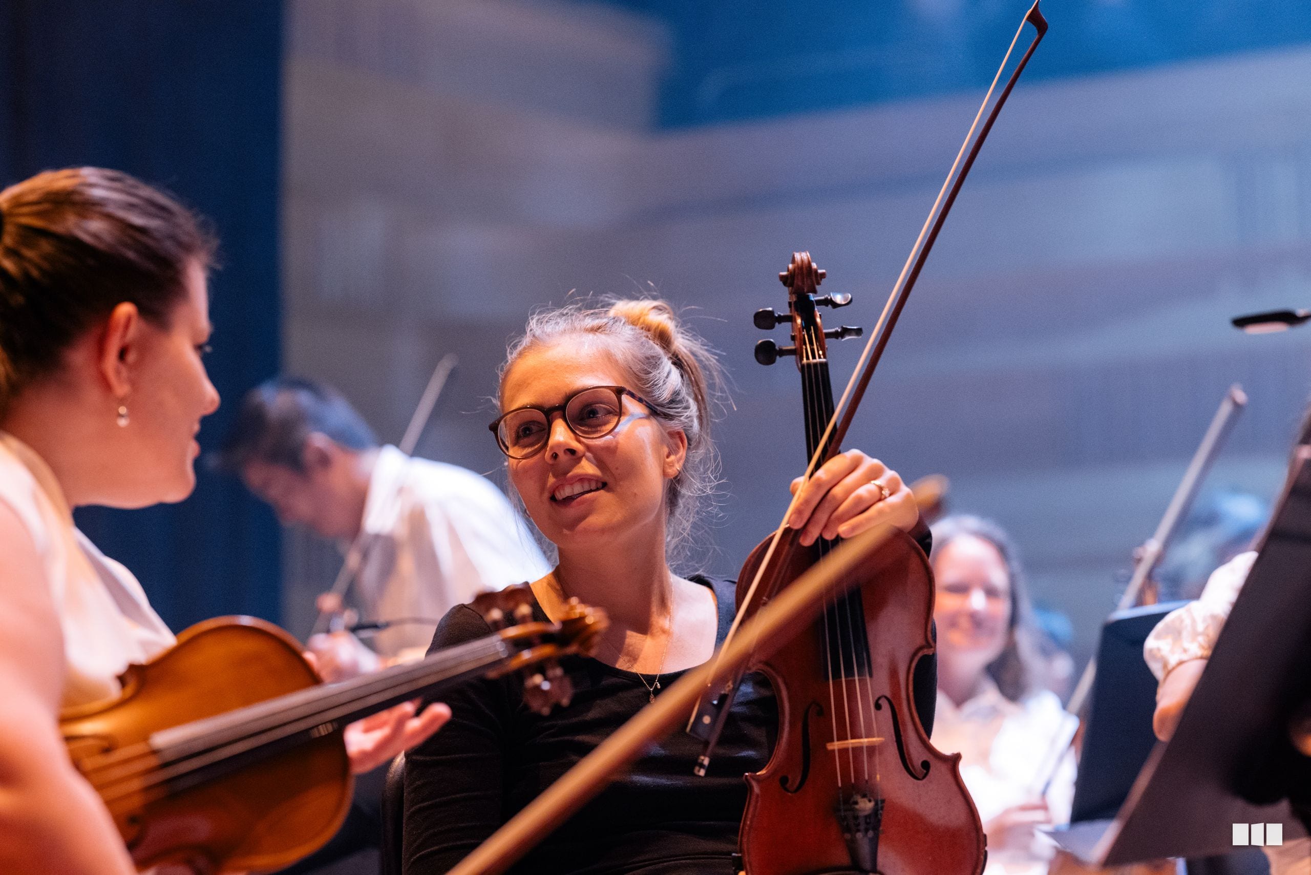 Young violinist with glasses performs alongside other string players during an orchestra rehearsal or performance.