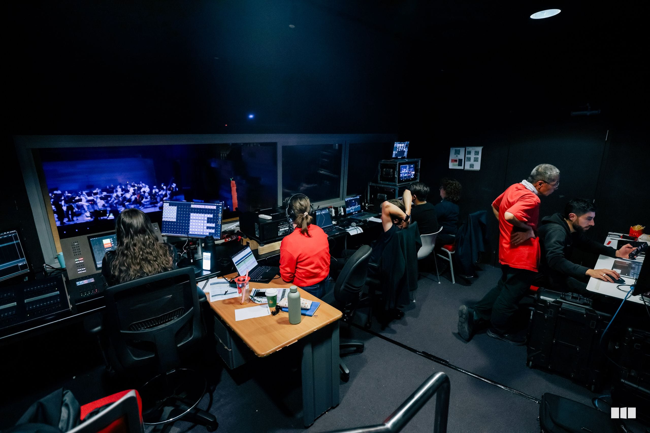 Technical crew monitors a live orchestral performance from the control room during a concert.