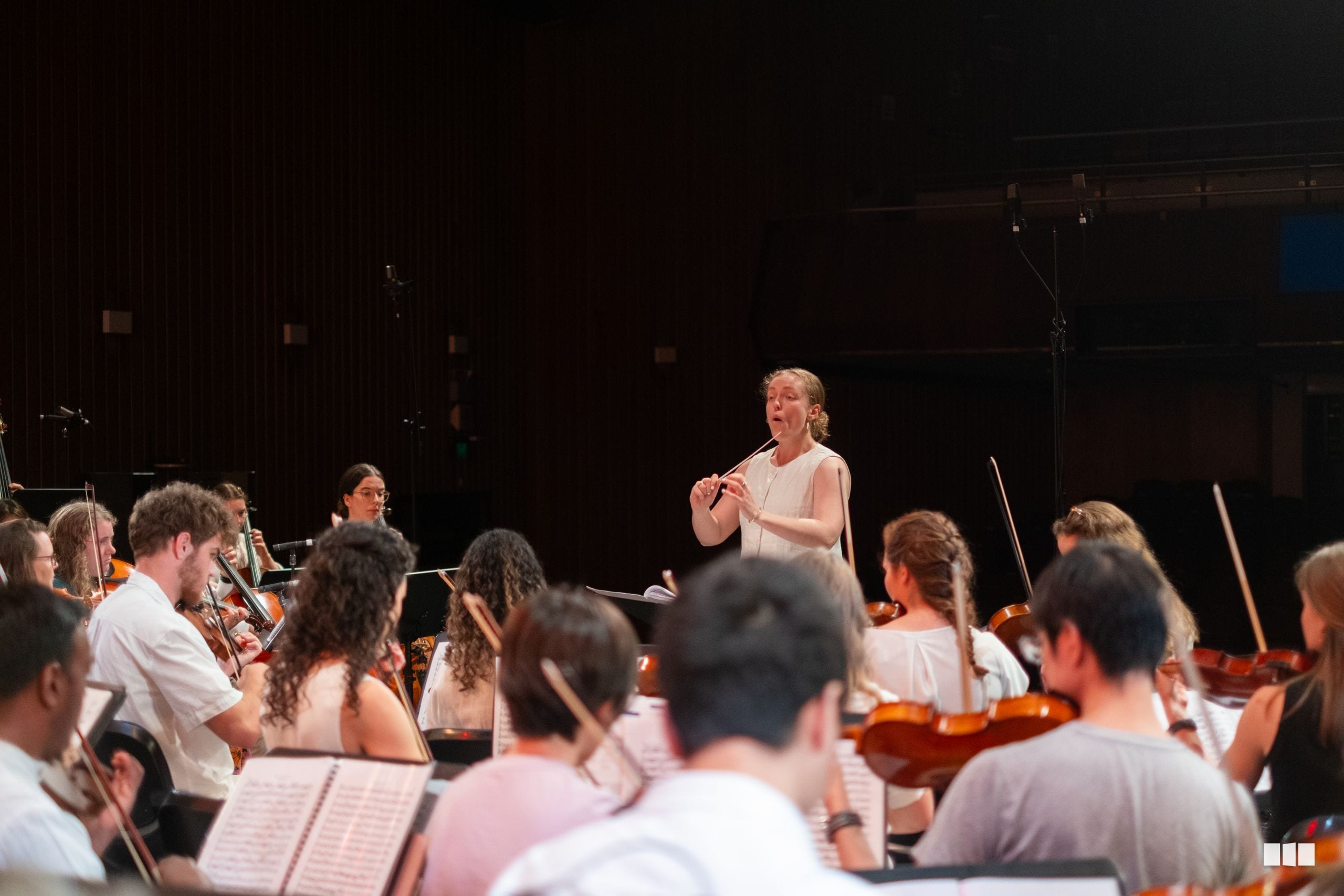A conductor leads a string orchestra section during a rehearsal or performance on stage.