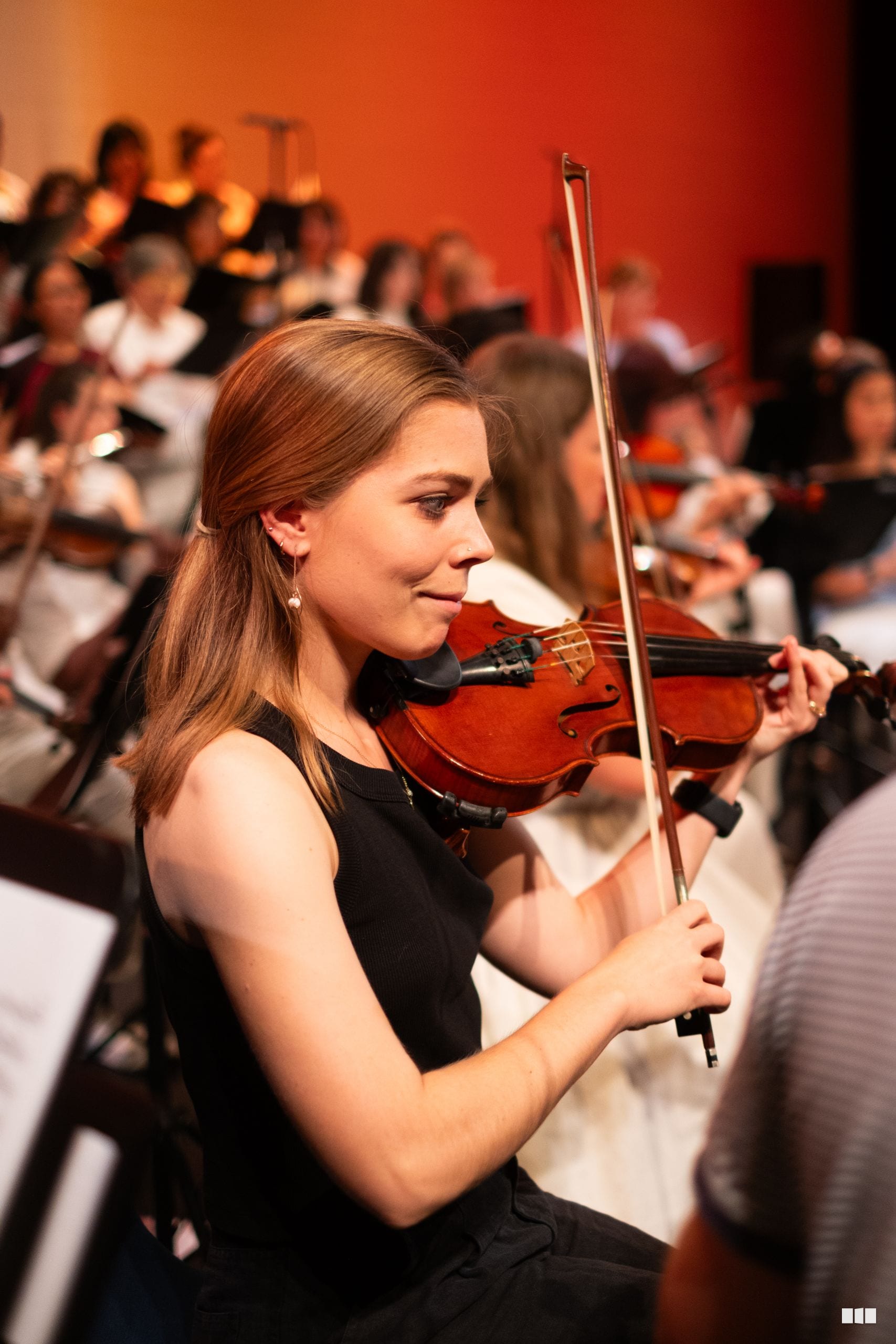 A violinist in formal black attire performs with focused concentration during an orchestral concert.