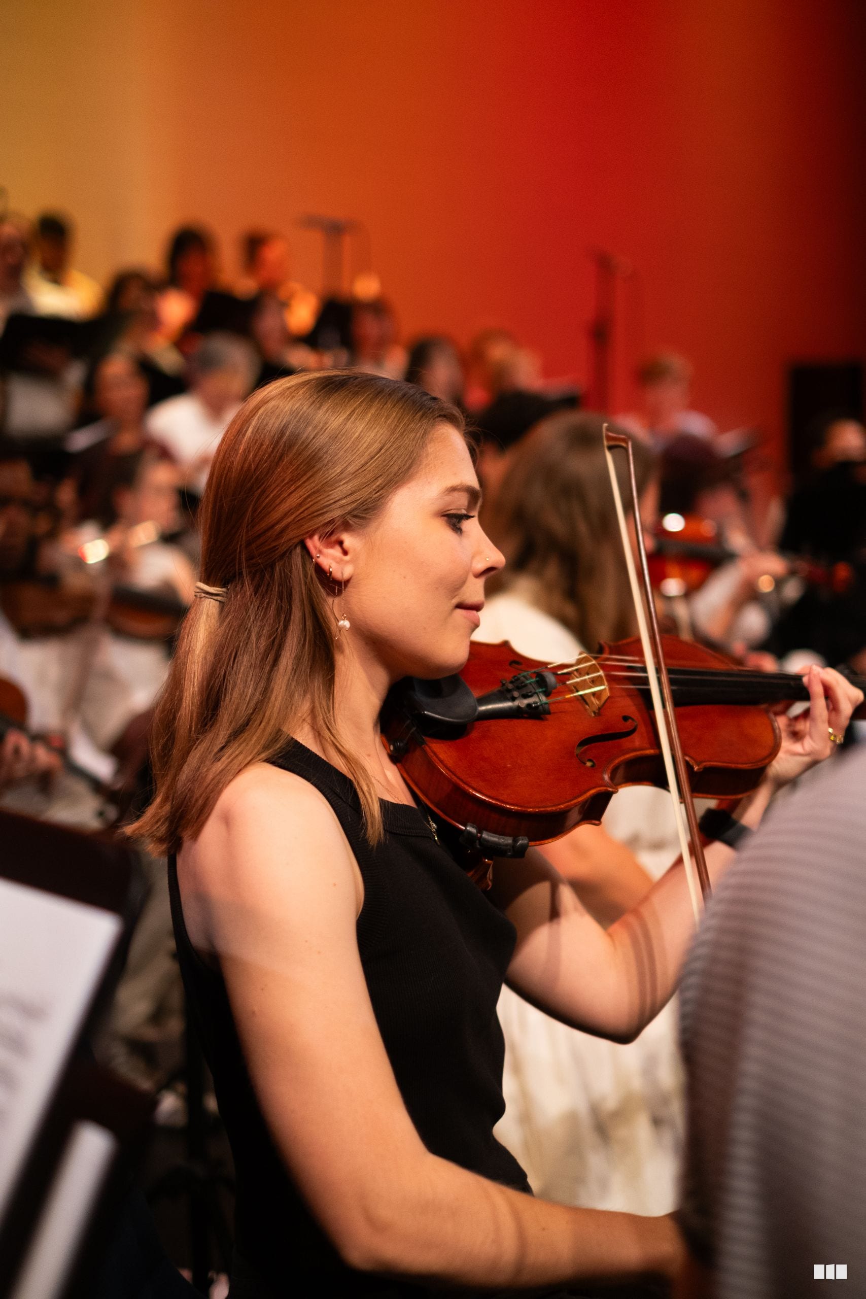 A young violinist in formal black attire performs with focused concentration during an orchestral concert.
