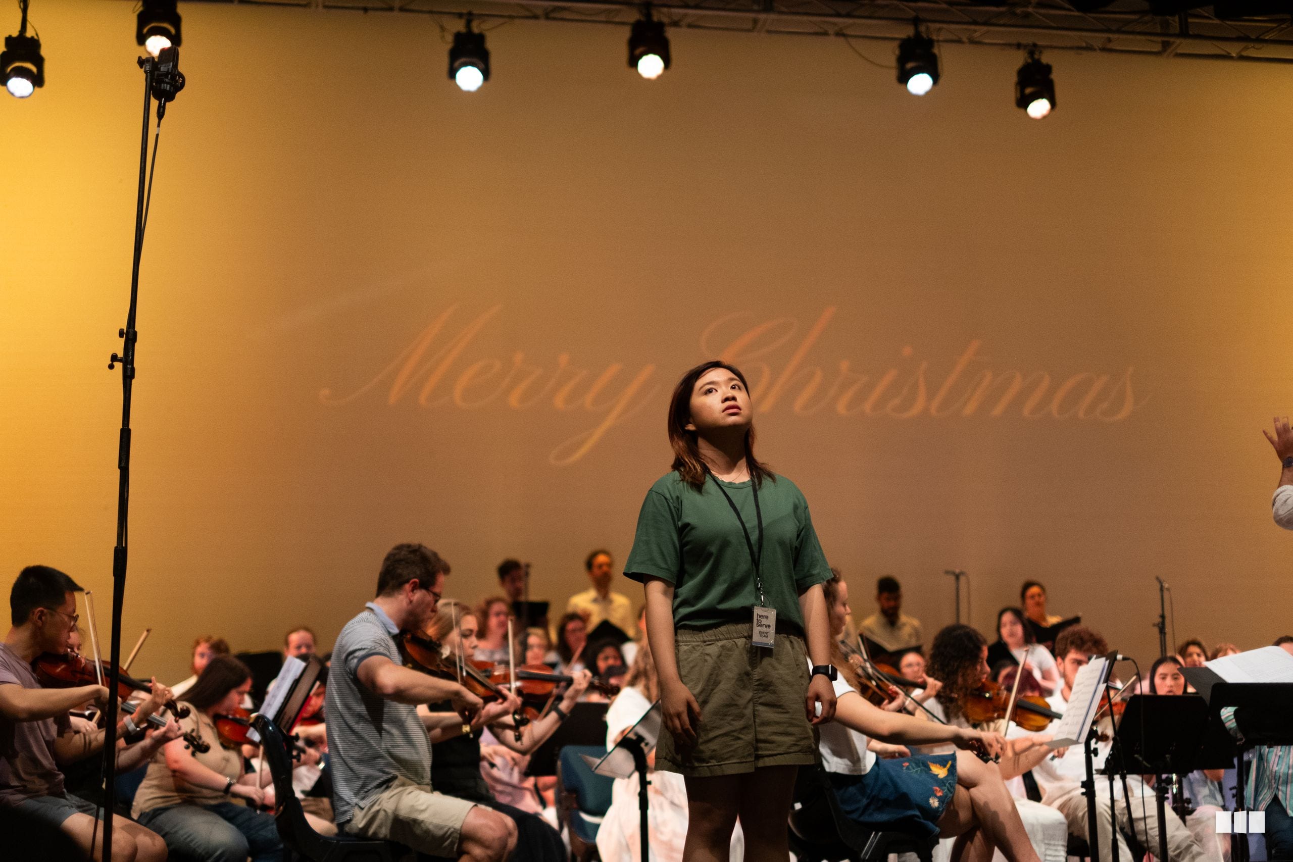 A young conductor leads a large ensemble of string players during a rehearsal or workshop session.