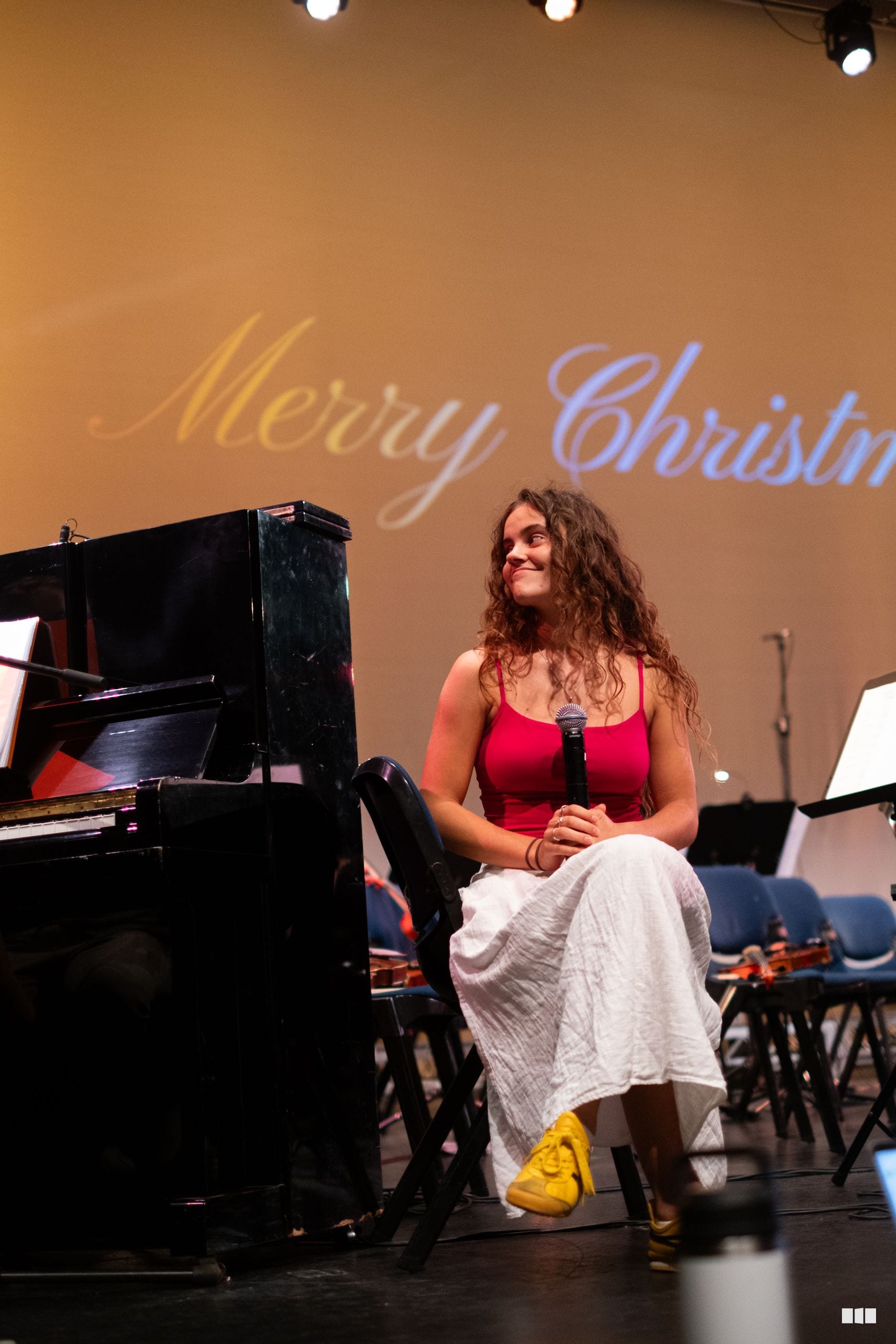 A soloist in a red top and white skirt performs at the microphone beside a grand piano during a Christmas concert.