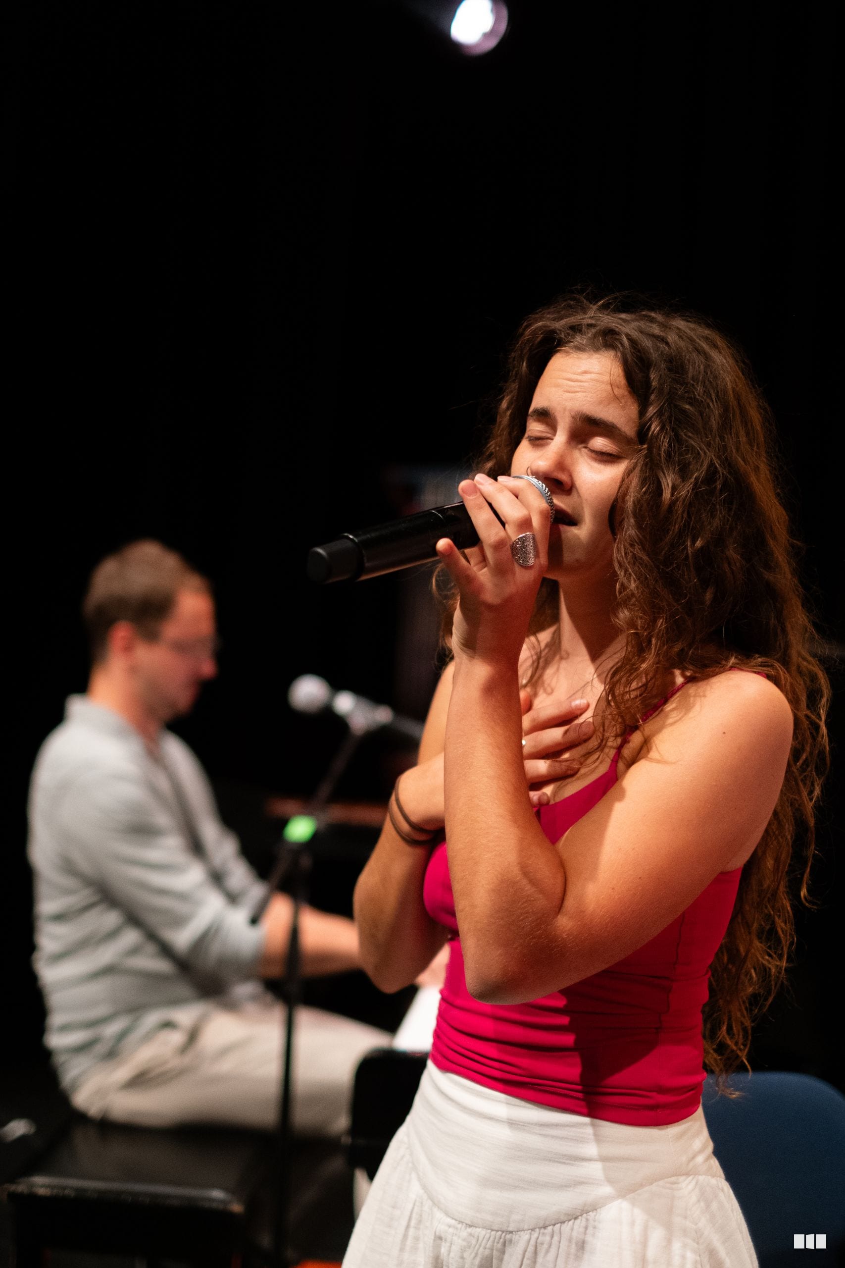 A female soloist performs with a microphone while a pianist accompanies her on stage.