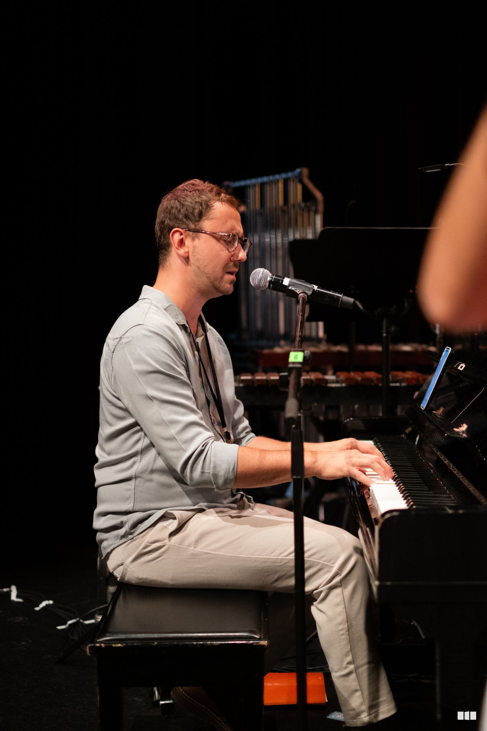 A male pianist performs at the keyboard while singing into a microphone during an orchestral concert.