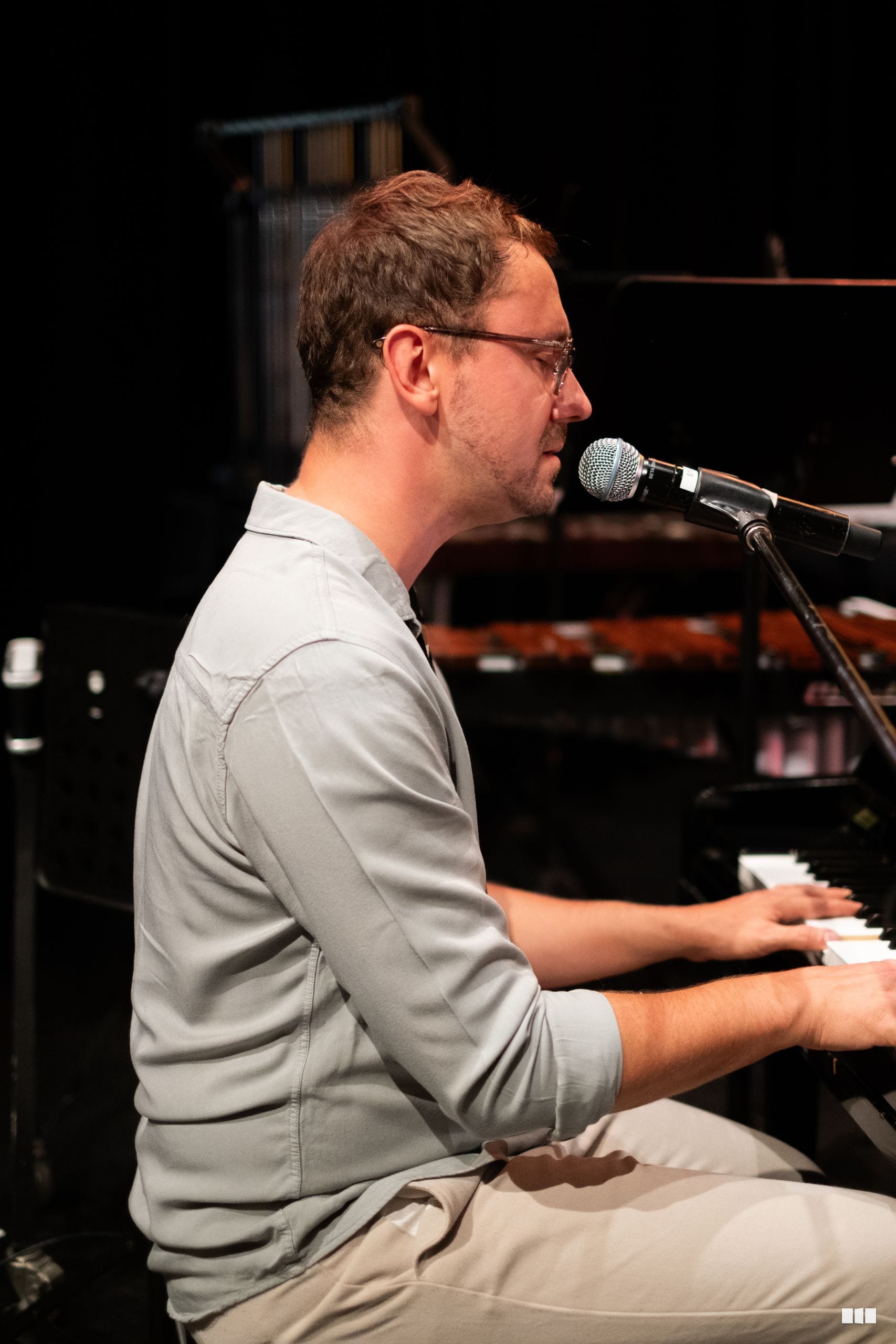 A musician performs at the piano while singing into a microphone during an orchestral performance.