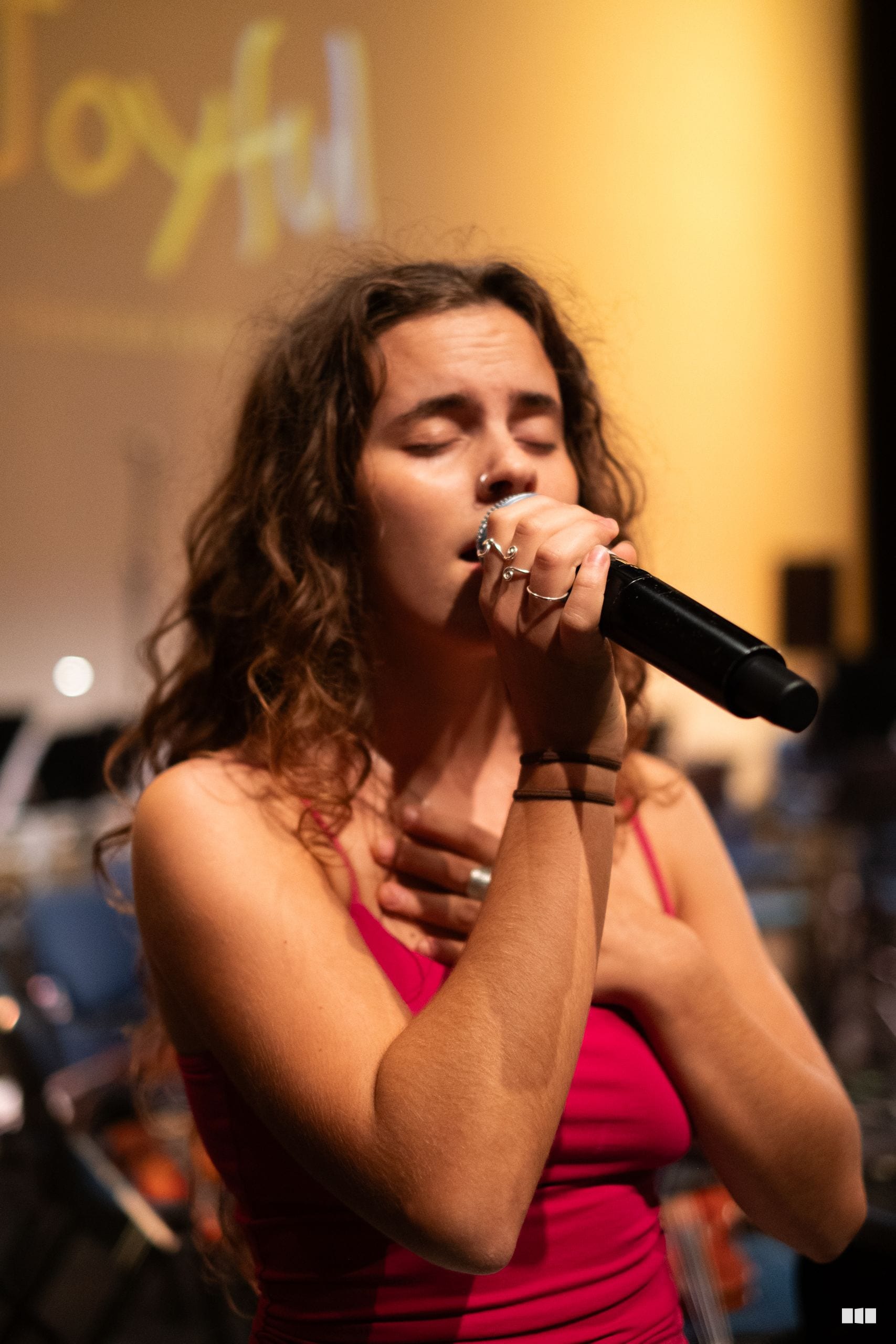 A female soloist in a pink dress performs passionately with a microphone during a choral performance.