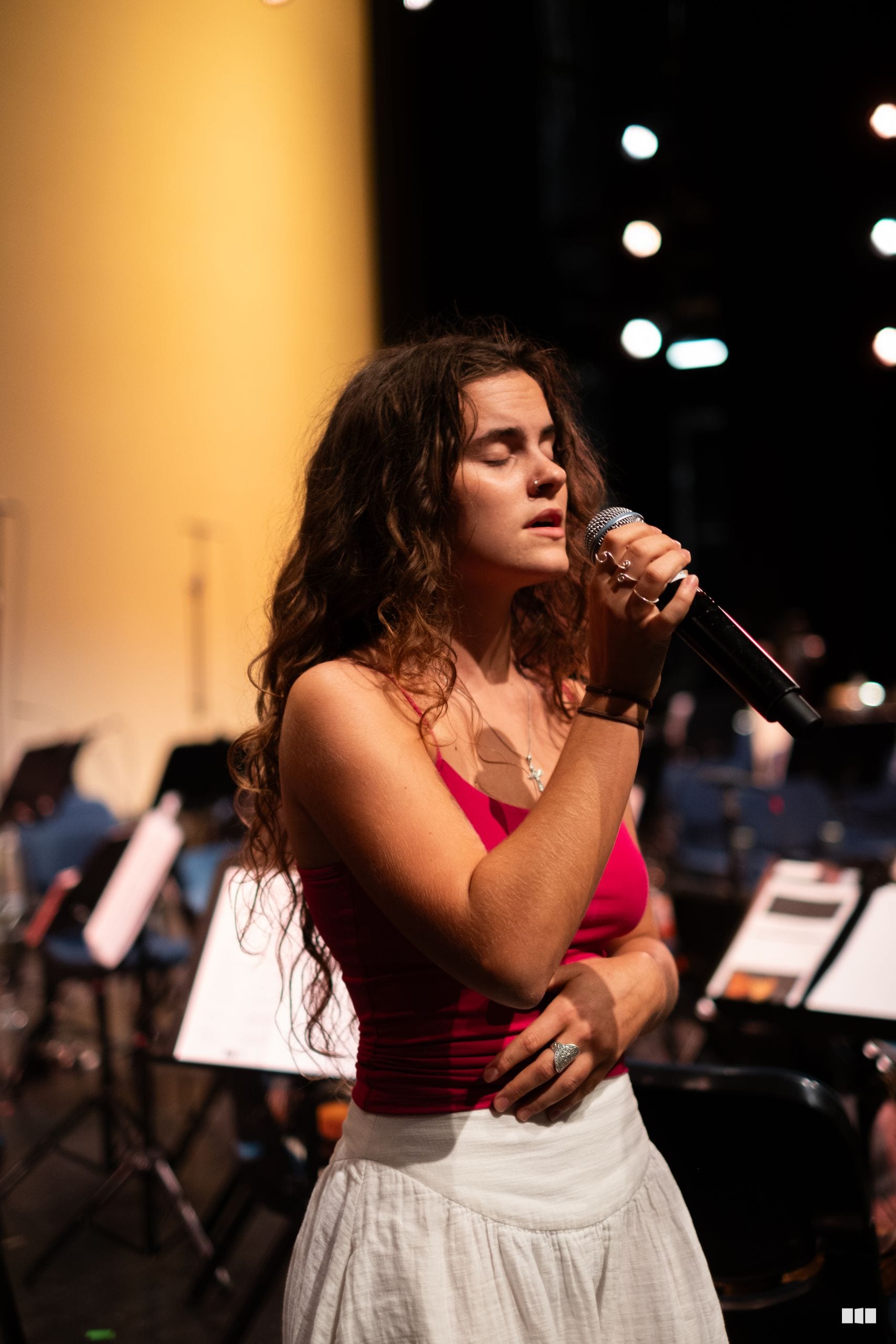 A young female soloist performs with a microphone during a choral or orchestral concert performance.