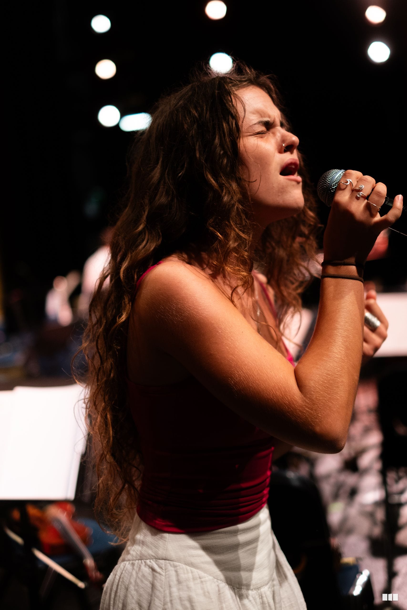 A female soloist performs passionately with a microphone on stage under stage lighting.