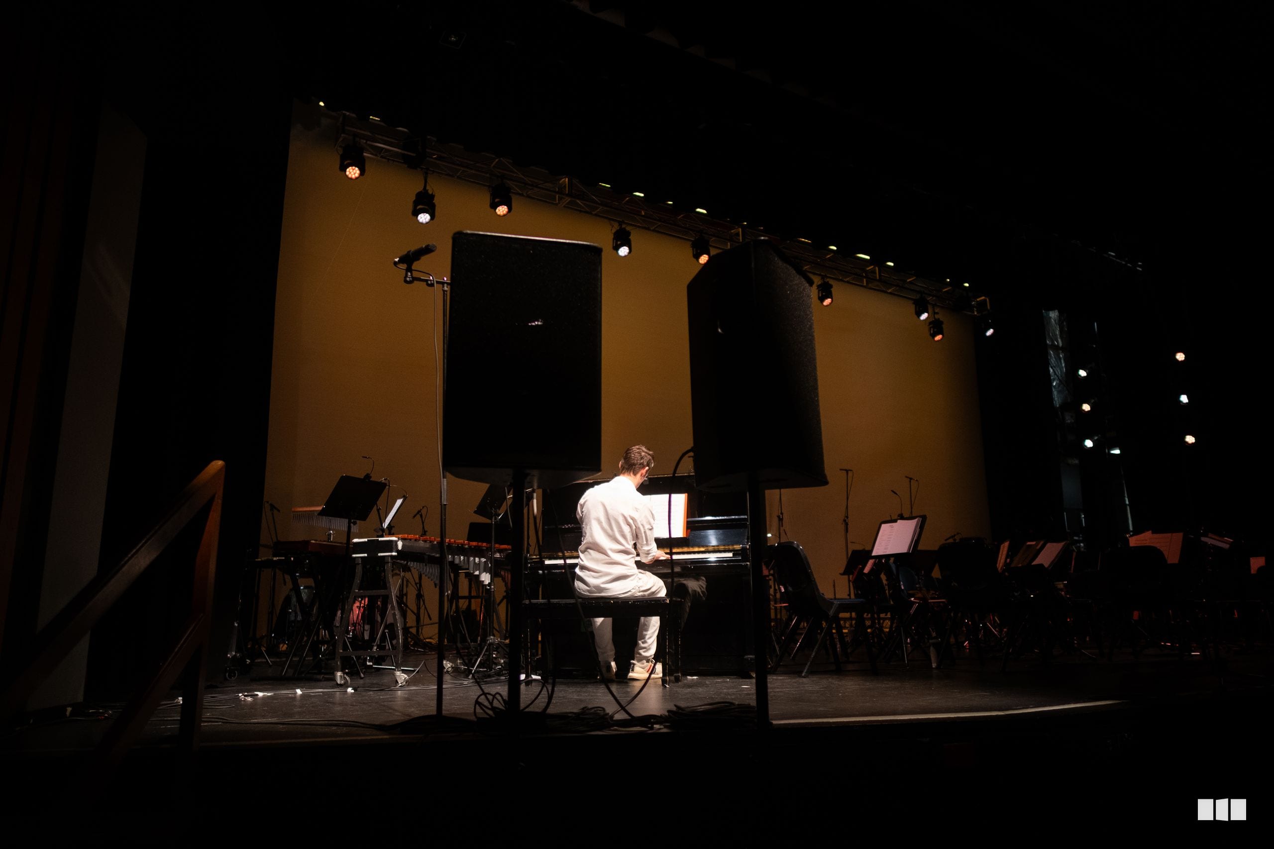 A pianist performs at the grand piano on stage during an orchestral concert, with musicians and equipment visible in the background.