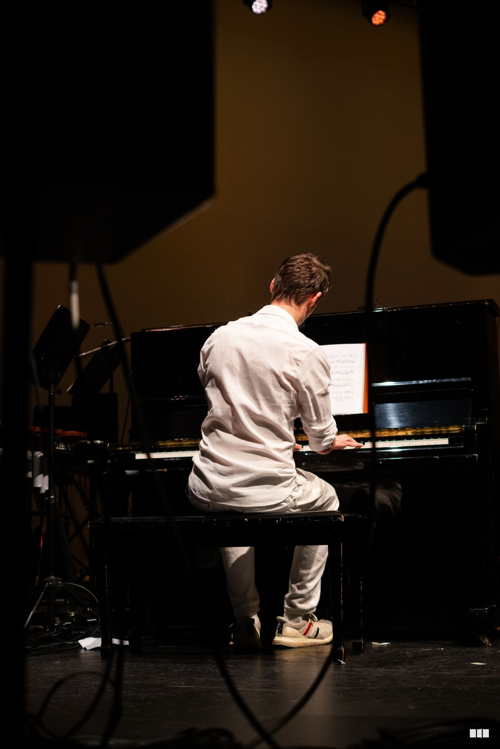 A pianist performs at the grand piano during an orchestral concert, reading from sheet music under stage lighting.