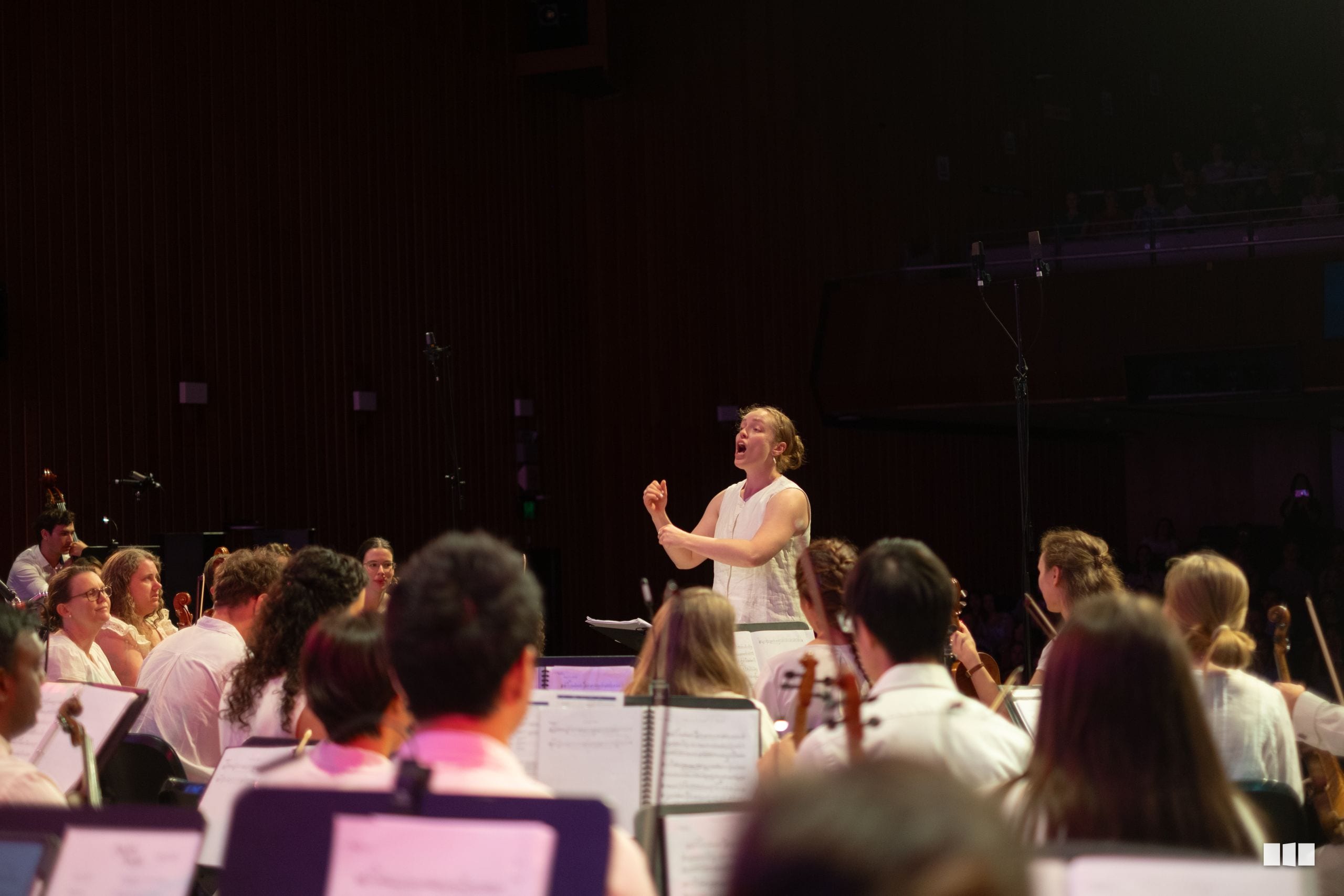 A conductor leads an orchestra and choir during a rehearsal or performance in a concert hall.