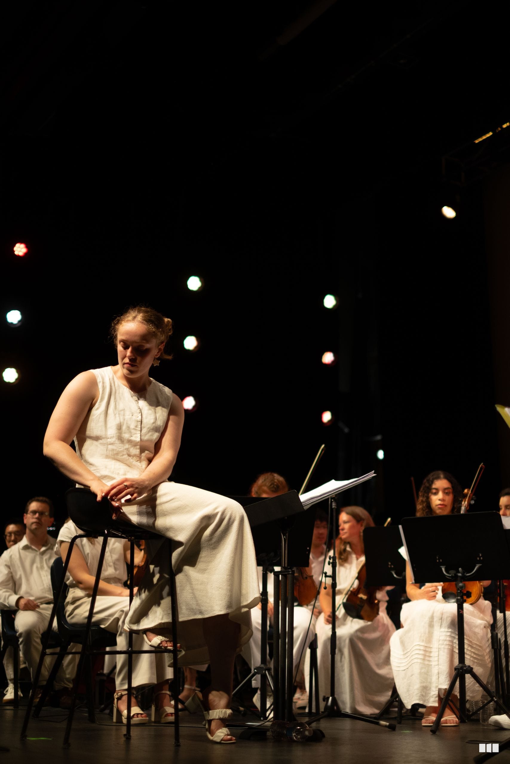 A young soloist performs on stage with orchestra members in white attire under stage lighting.