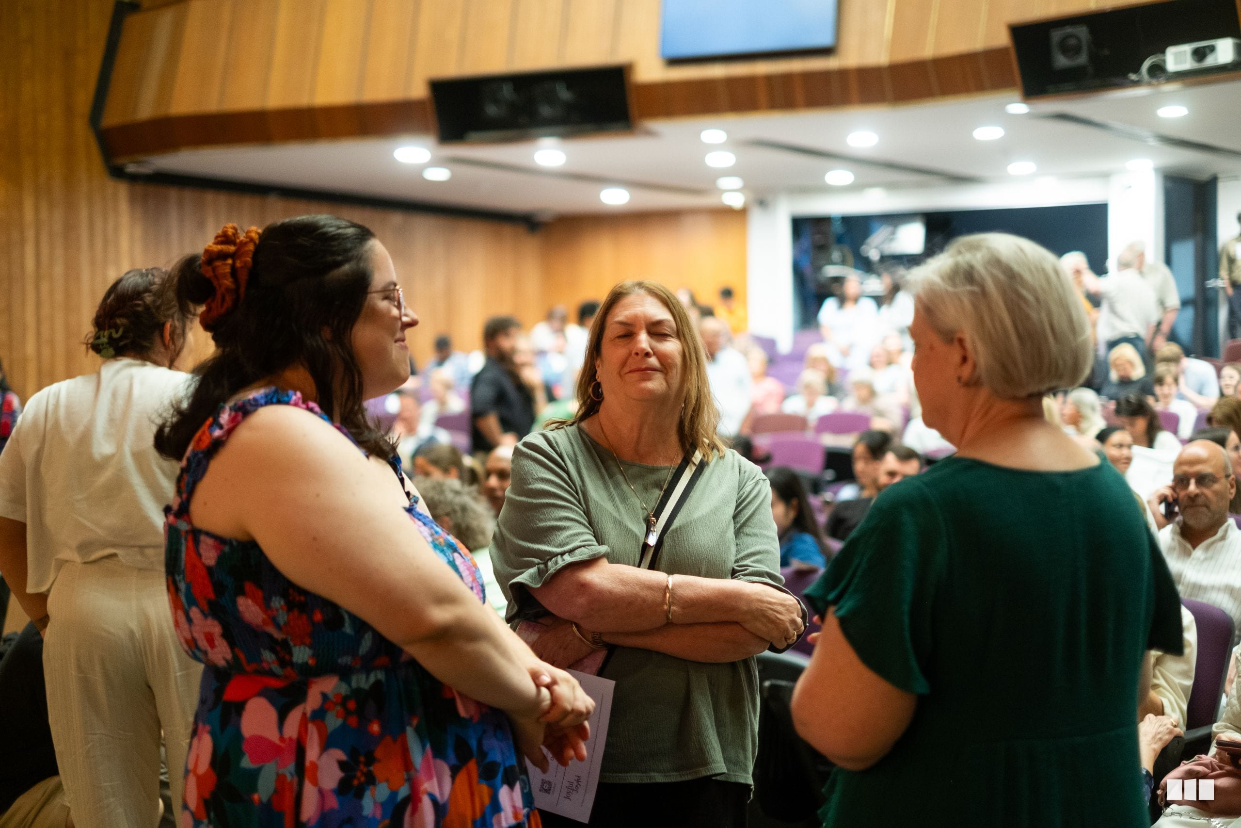 Staff members engage in conversation with audience members in the auditorium during an event.