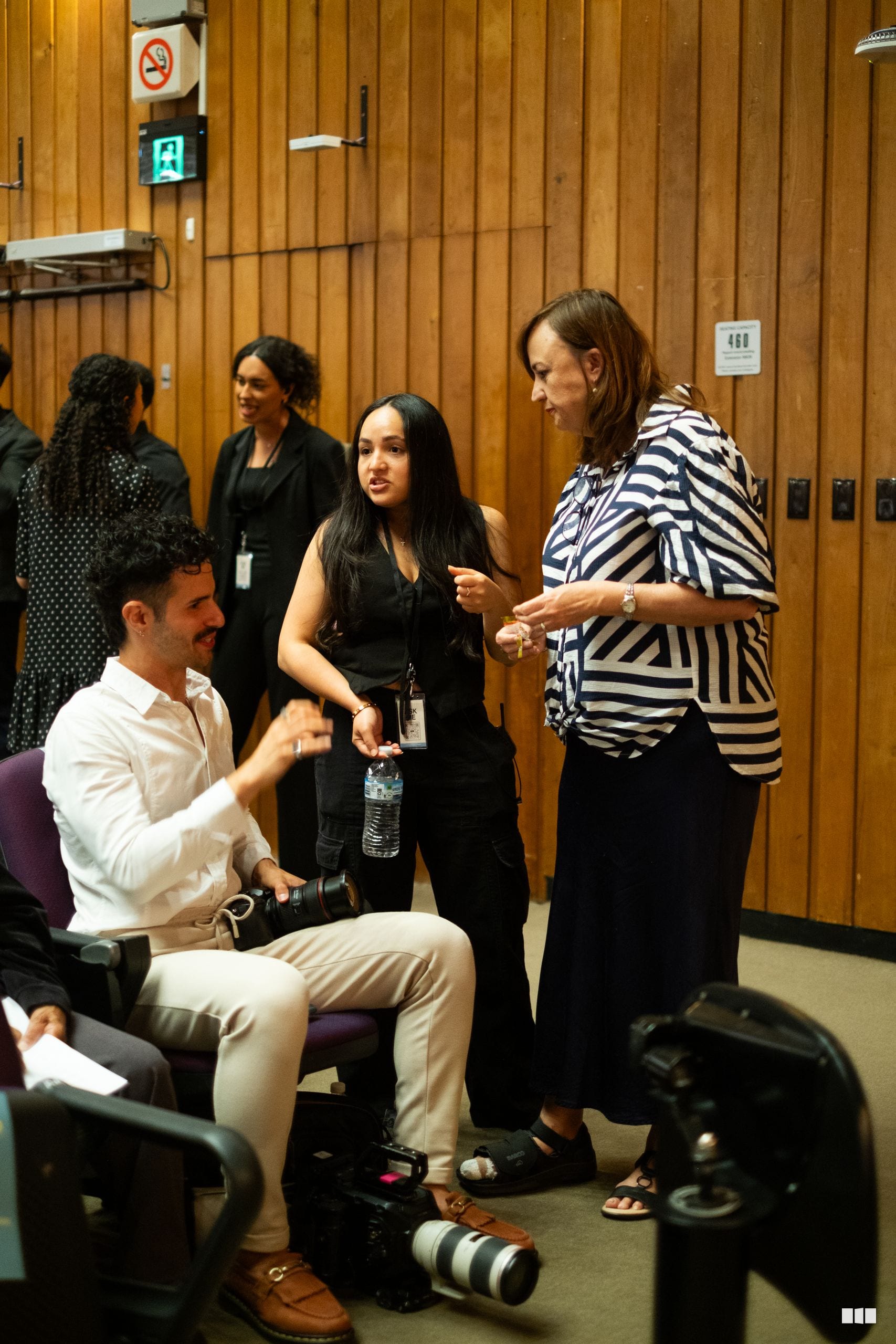 Professional team members engage in conversation at an indoor event venue with wooden paneling.