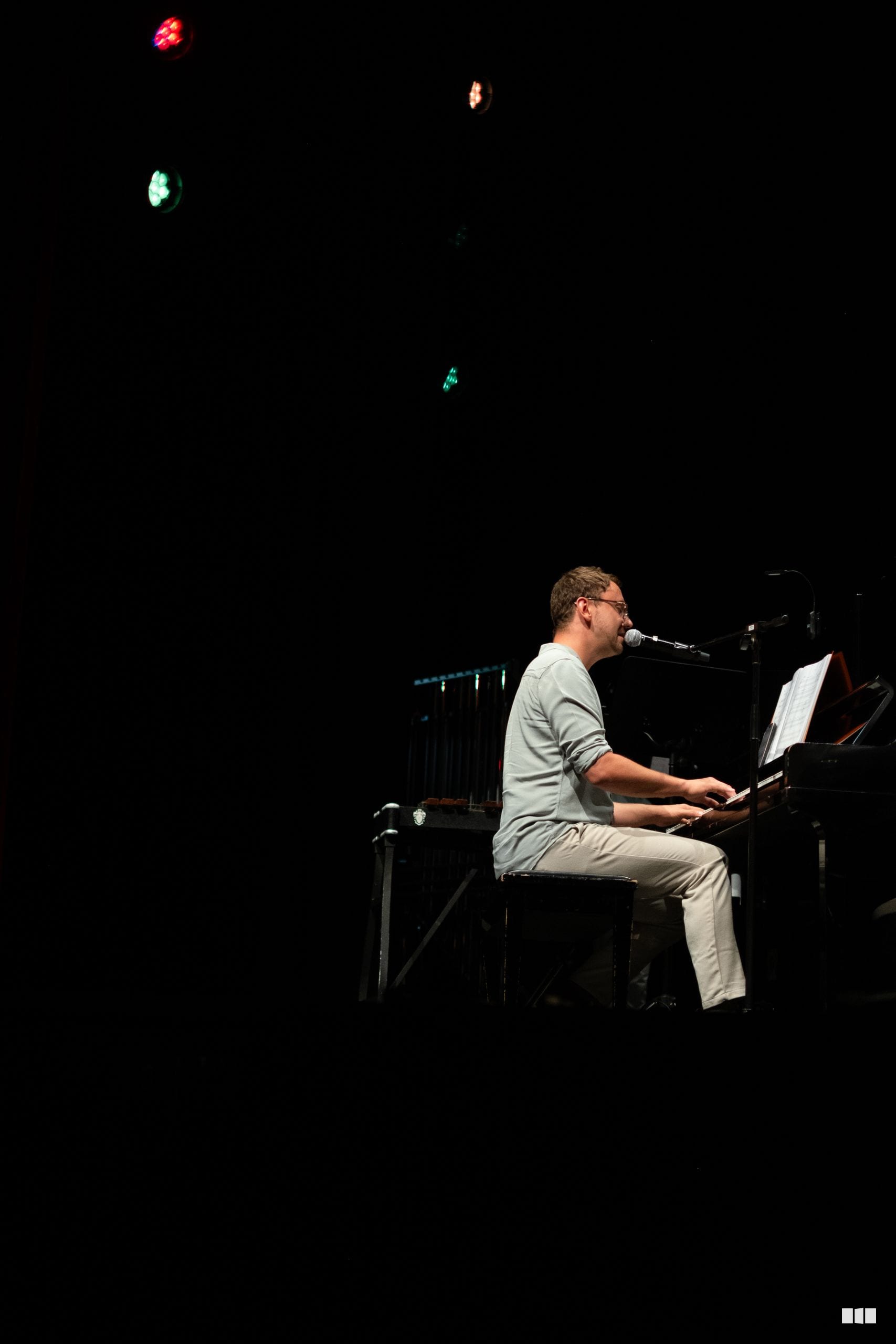 A musician performs at the piano while singing into a microphone during an orchestral performance.