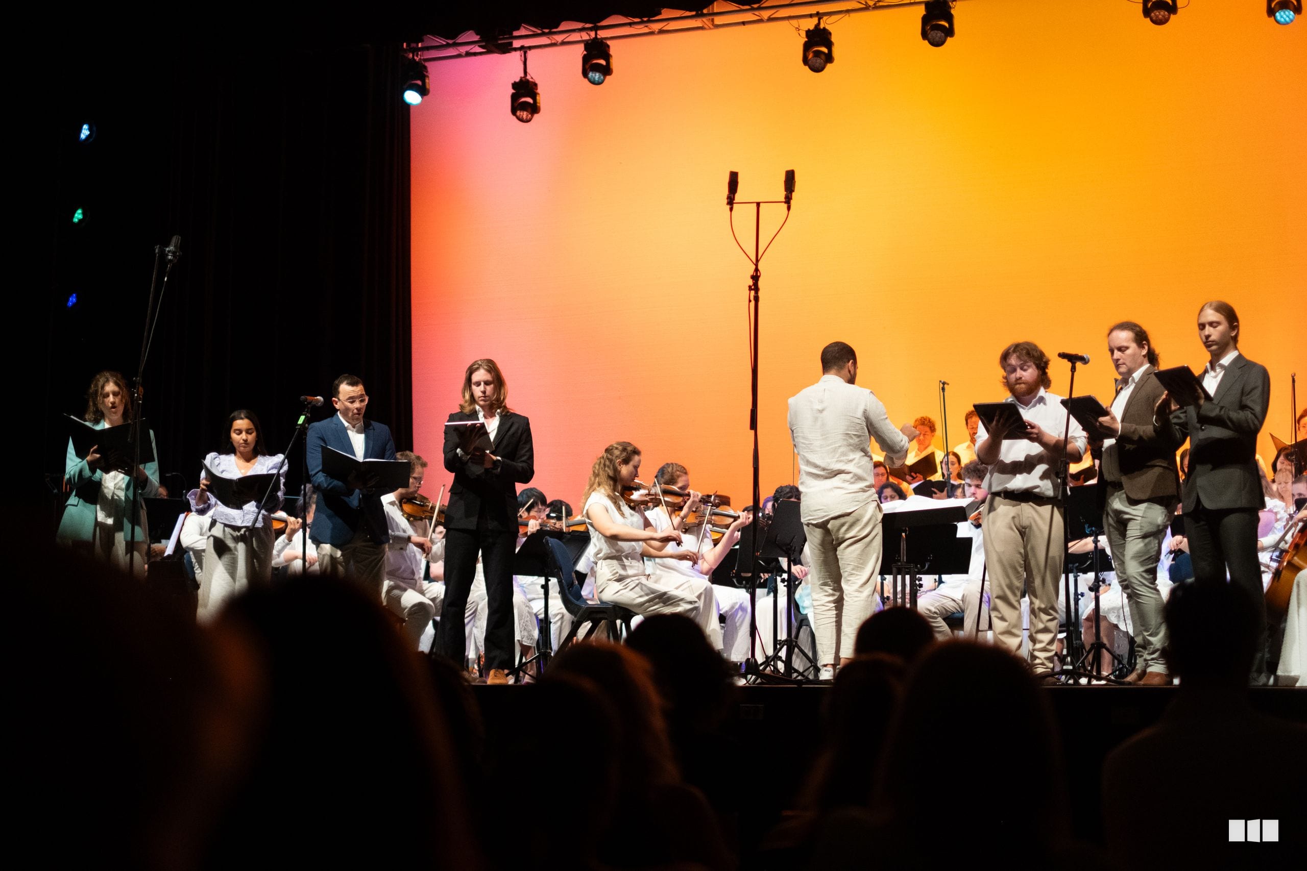 Orchestra and choir members take a bow together on stage under warm amber lighting after a performance.