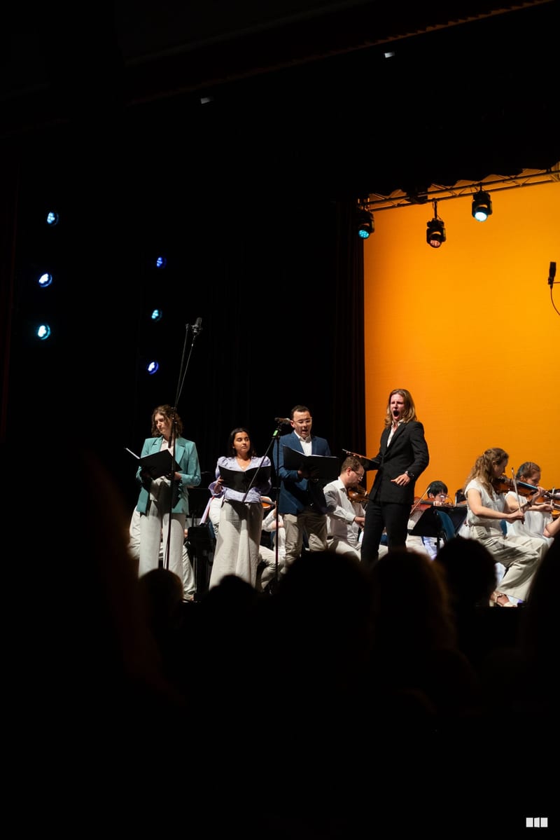 Soloists and orchestra members perform together on stage with sheet music under stage lighting.
