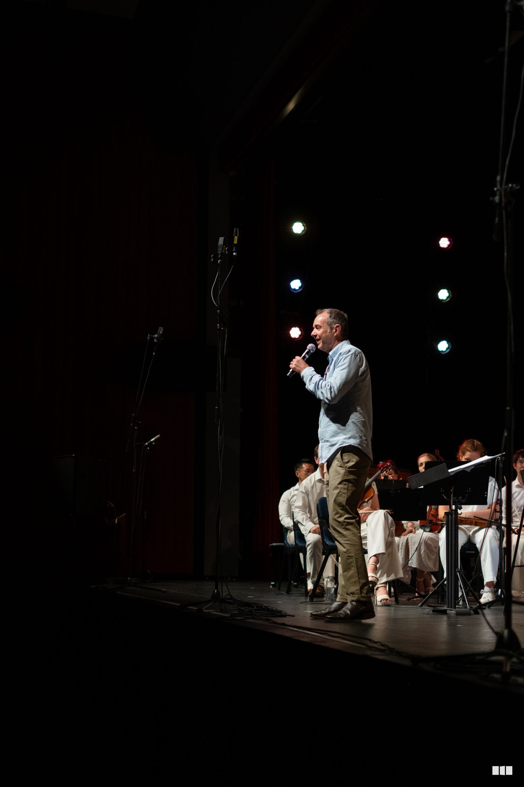 A male soloist performs at the microphone while seated musicians accompany him on stage.