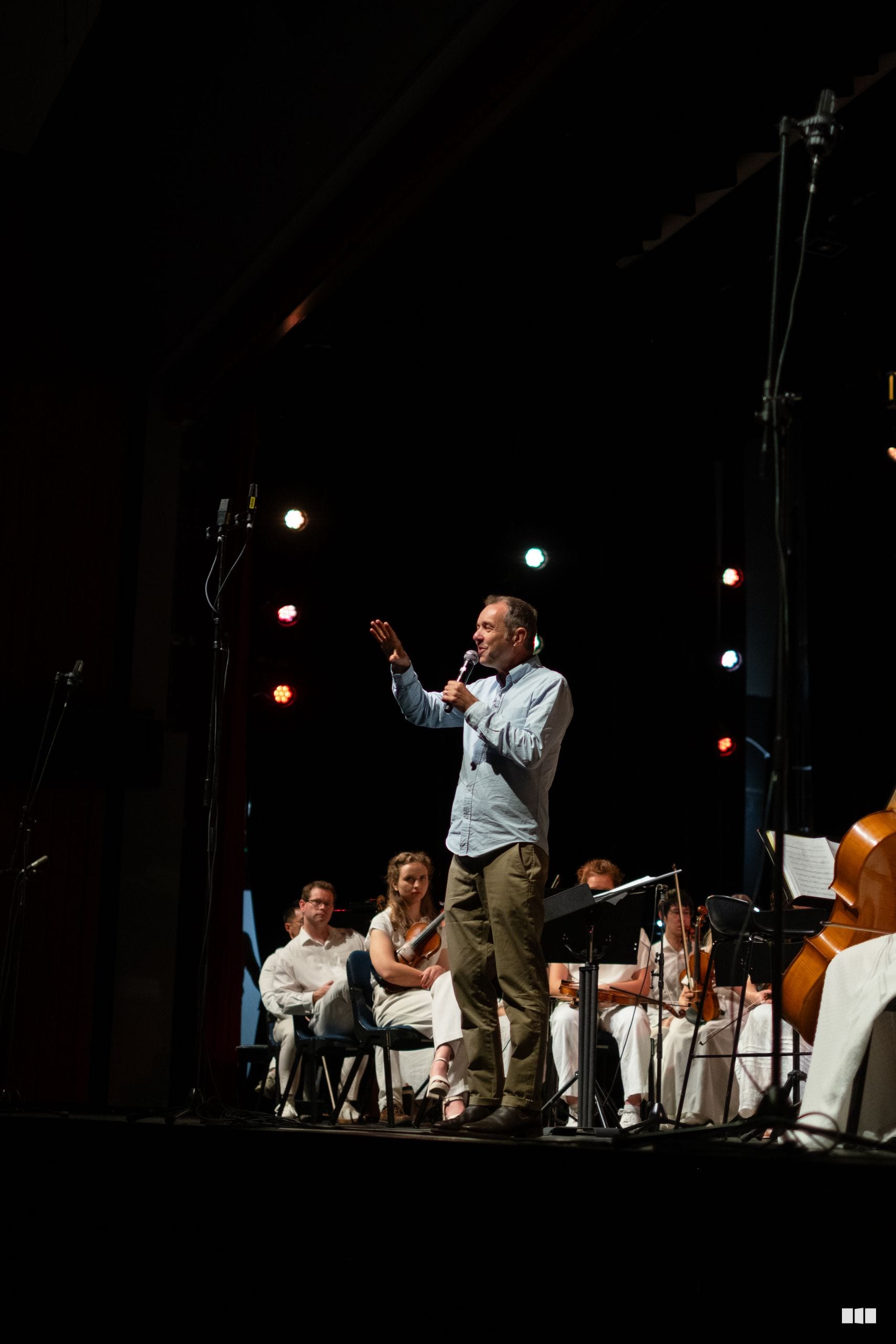 A conductor gestures expressively while leading musicians during an orchestral performance on stage.