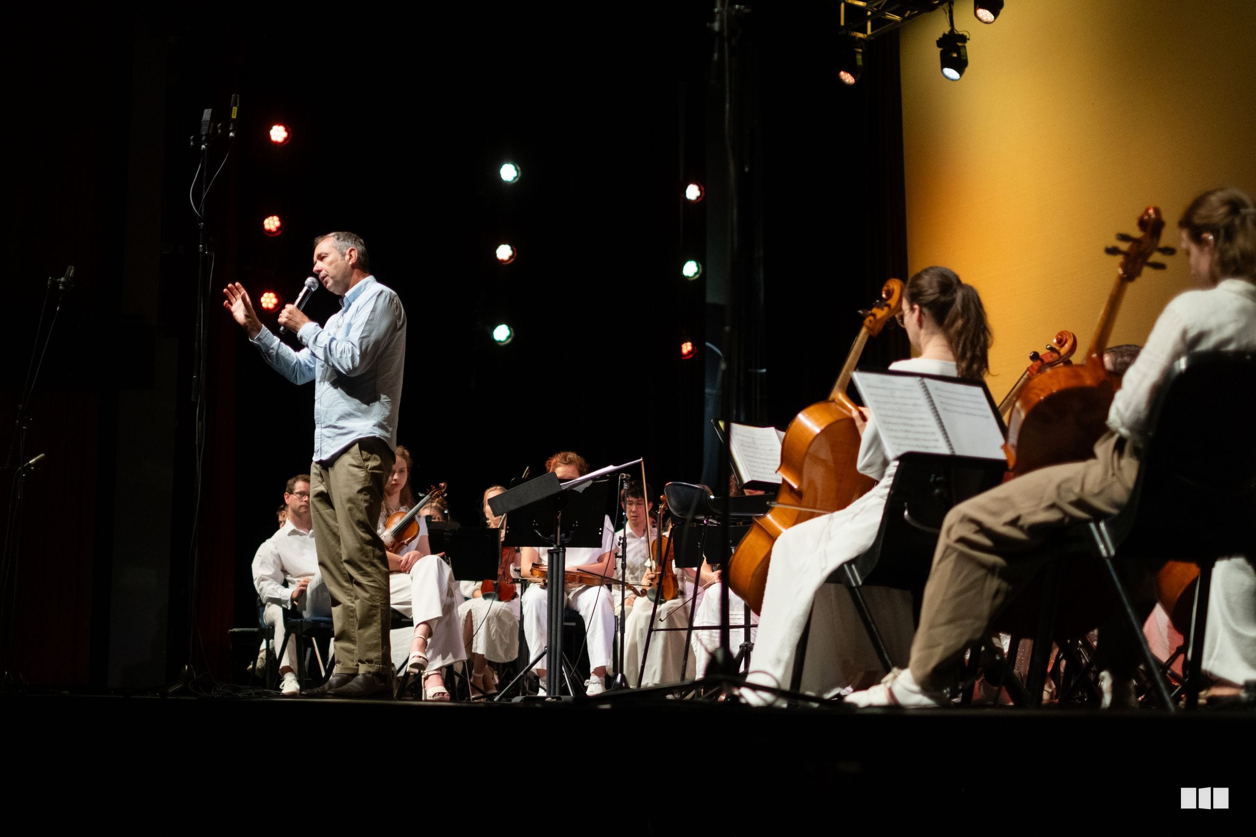 A conductor leads a string orchestra during a performance on stage with professional lighting.