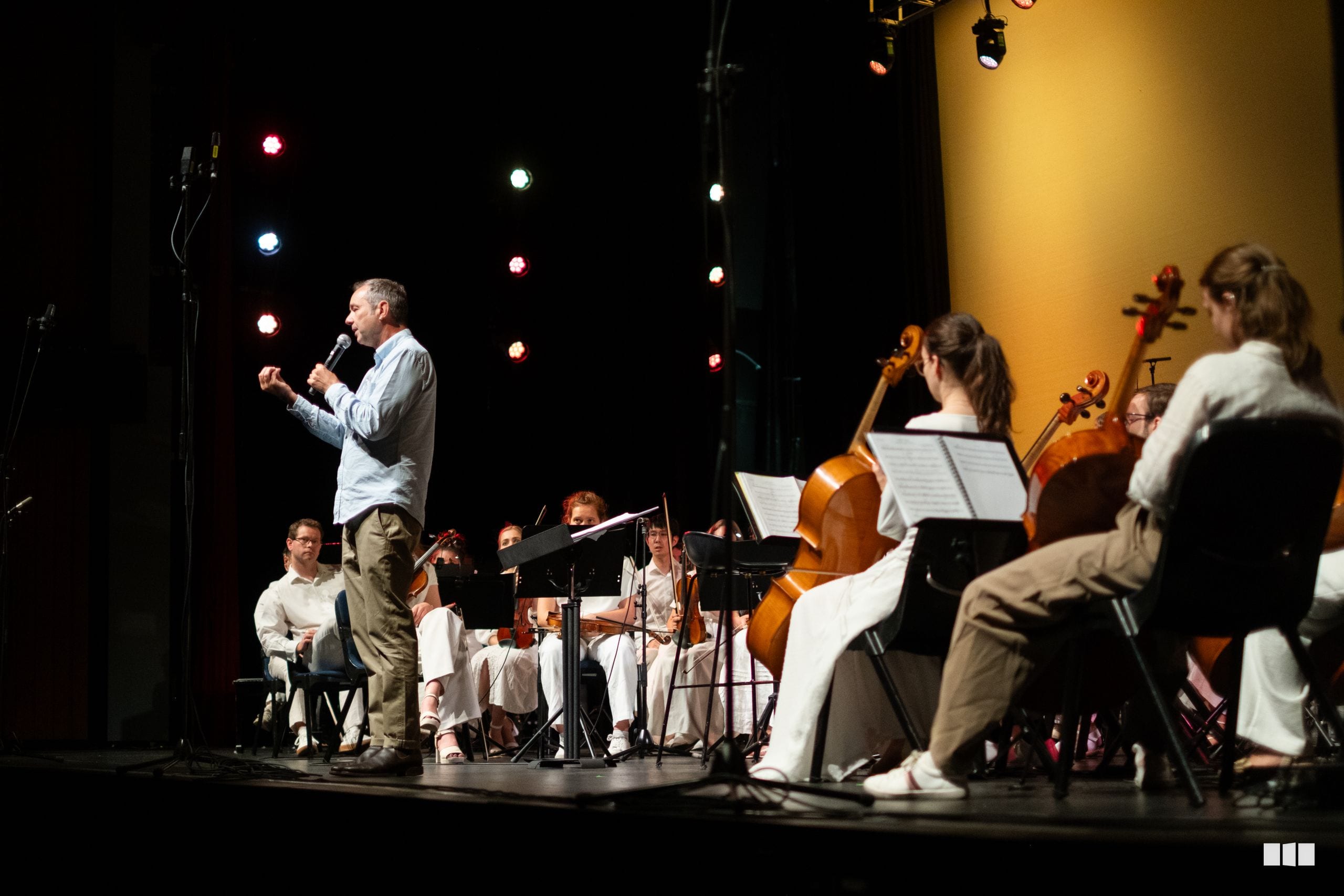 A conductor leads a string orchestra during a performance on stage with professional lighting.