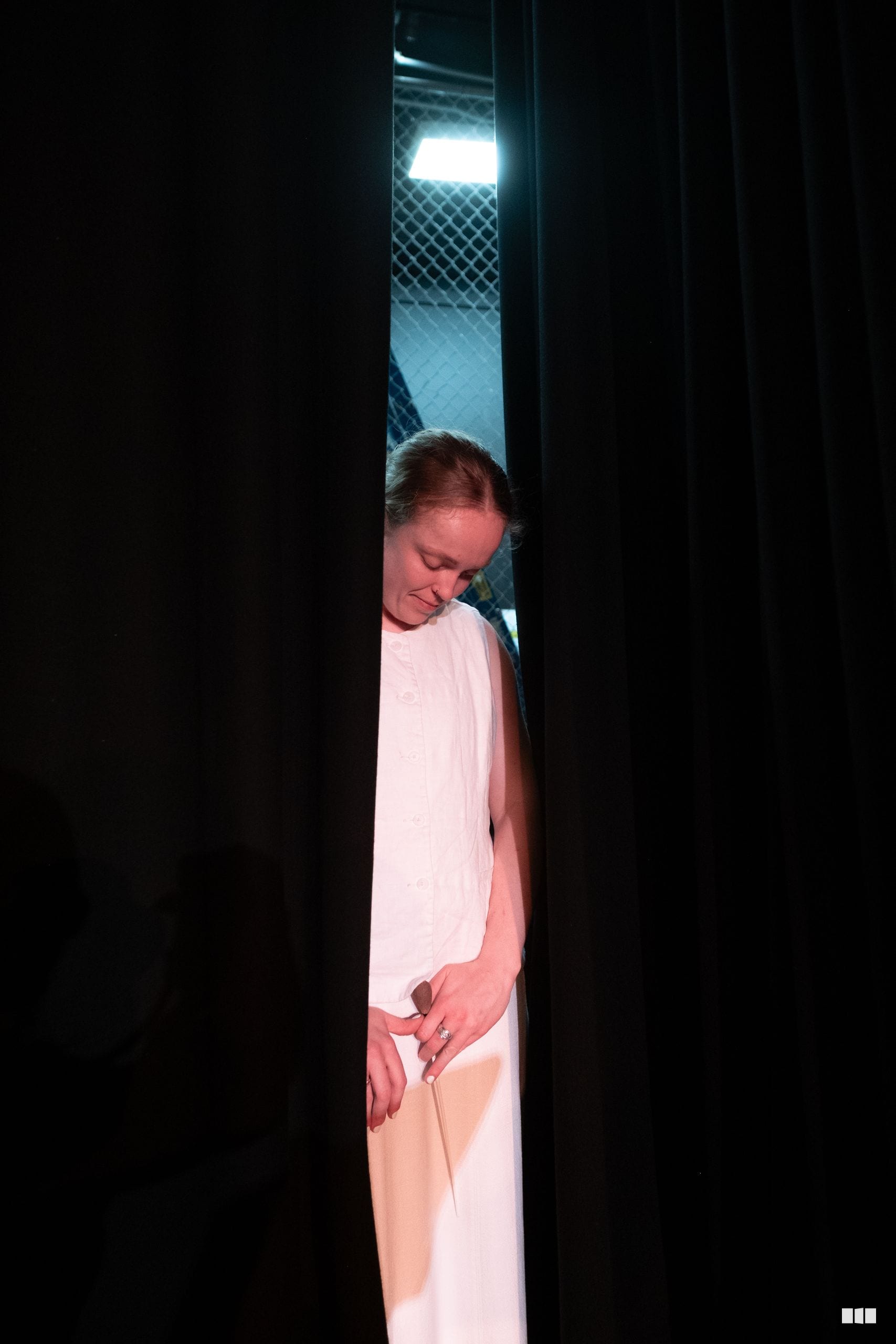 A person in white clothing stands in a doorway with stage lighting visible above.