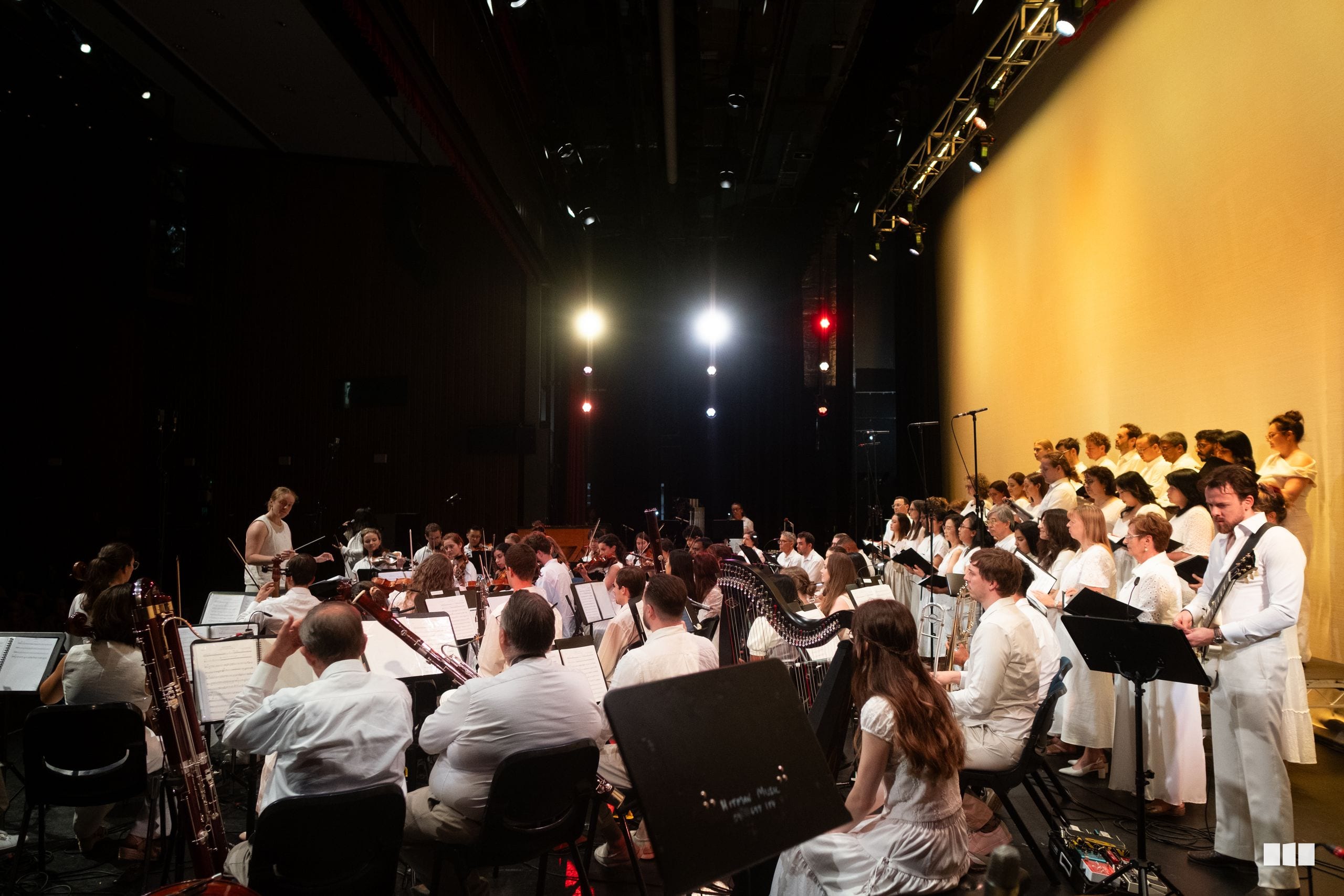 Orchestra and choir perform together on stage with full ensemble arrangement under professional stage lighting.