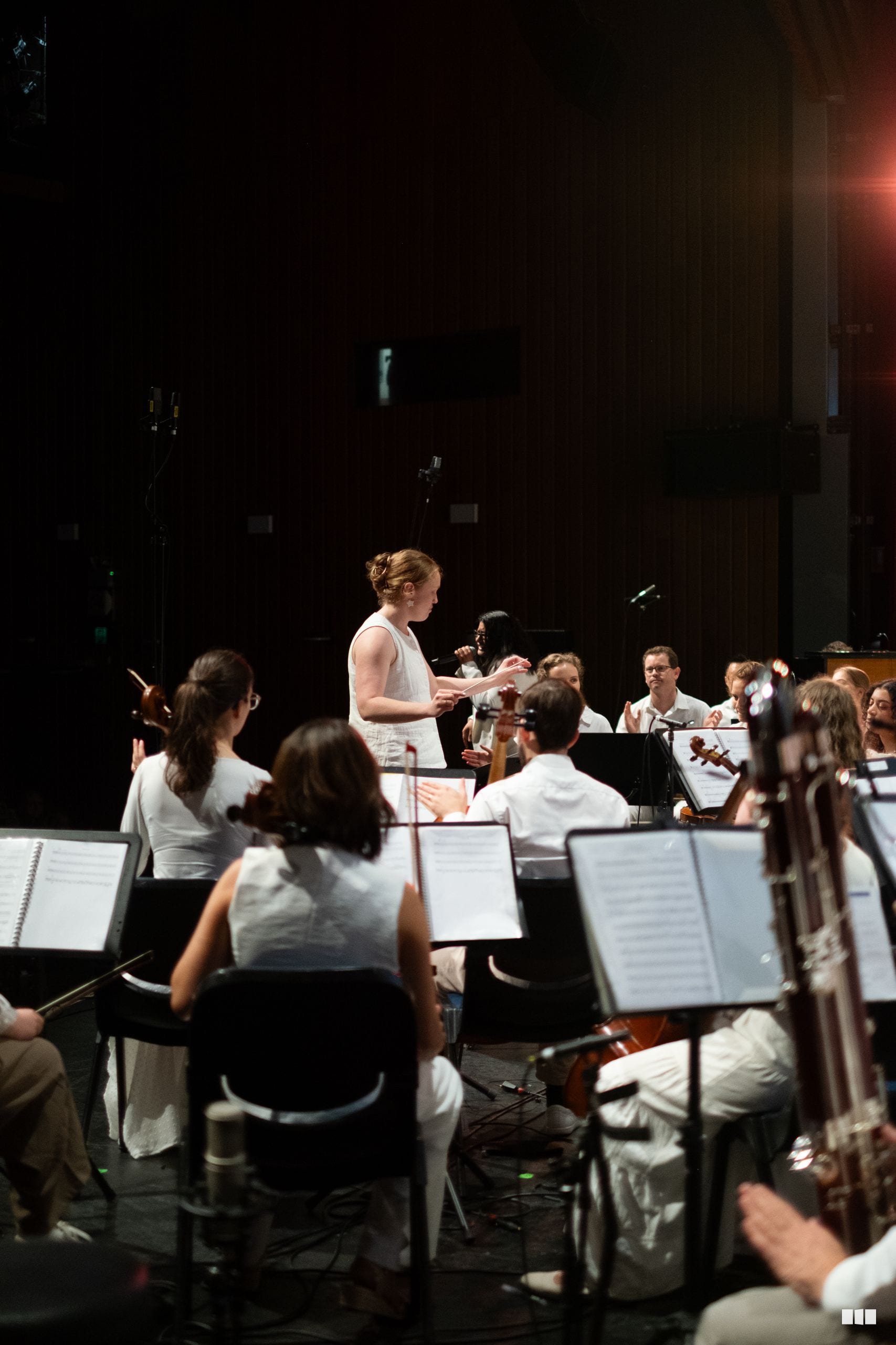 A conductor leads a string orchestra section during a rehearsal or performance on stage.